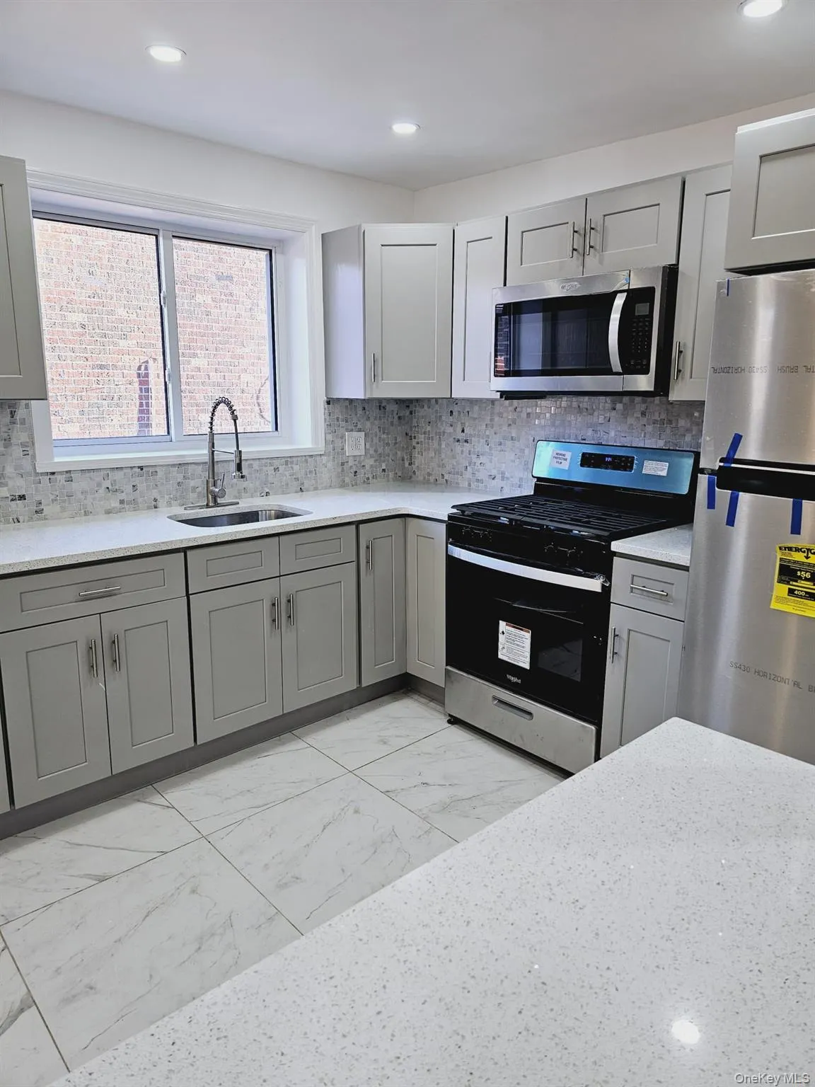 Kitchen with stainless steel appliances, light marble finish floors, gray cabinets, backsplash, and recessed lighting Kitchen with stainless steel appliances, light marble finish floors, gray cabinets, backsplash, and recessed lighting