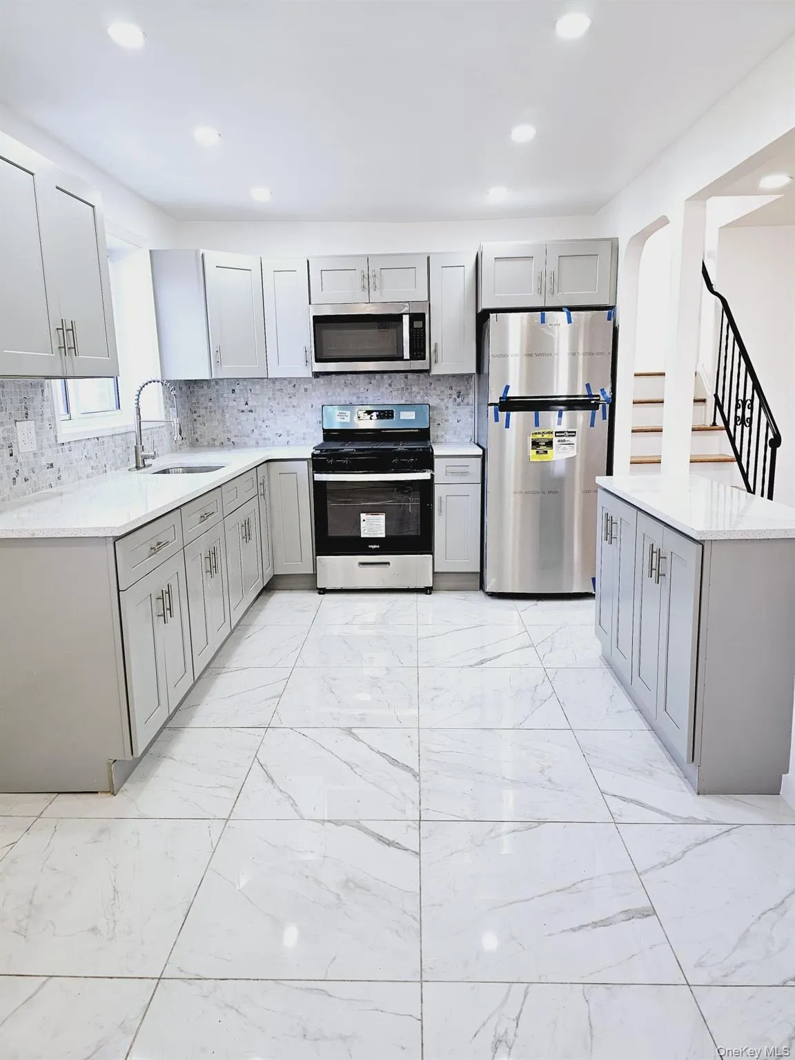Kitchen featuring appliances with stainless steel finishes, light stone counters, gray cabinetry, light marble finish flooring, and recessed lighting Kitchen featuring appliances with stainless steel finishes, light stone counters, gray cabinetry, light marble finish flooring, and recessed lighting