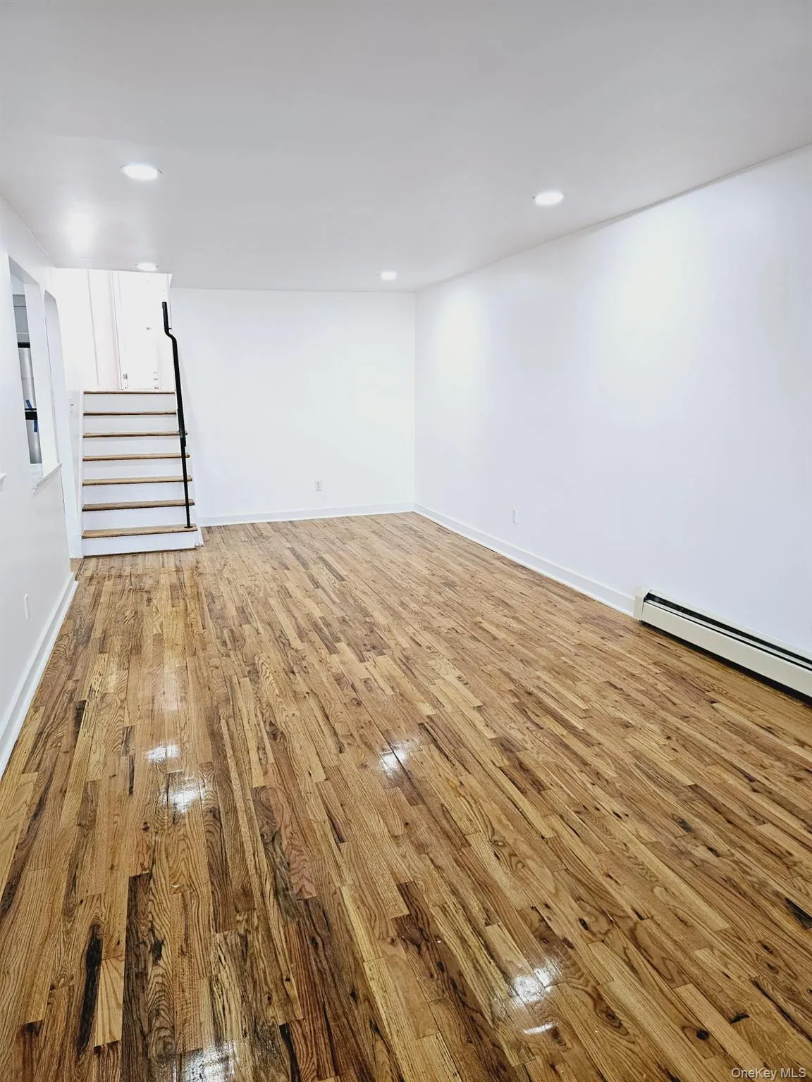 Empty room with a baseboard heating unit, stairway, light wood-style floors, and recessed lighting Empty room with a baseboard heating unit, stairway, light wood-style floors, and recessed lighting