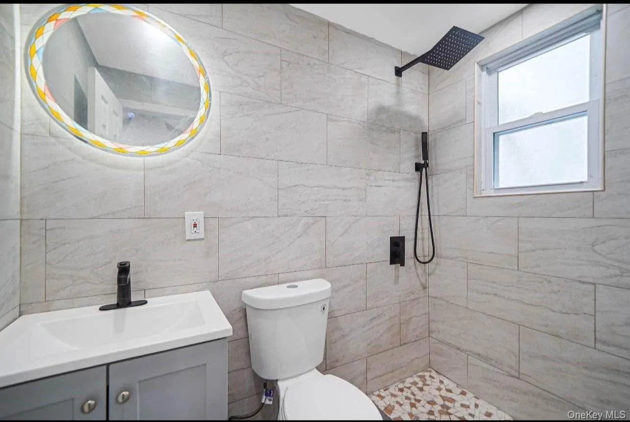 Bathroom featuring vanity, a tile shower, and tile walls Bathroom featuring vanity, a tile shower, and tile walls
