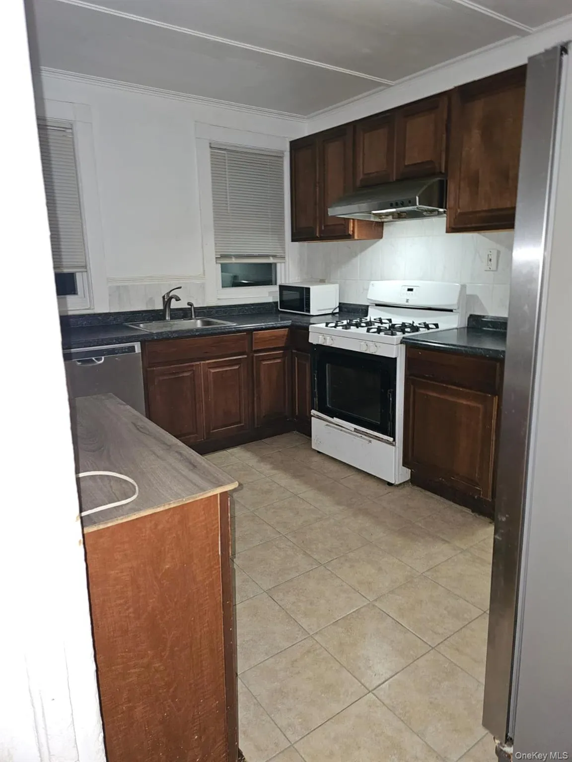 Kitchen featuring appliances with stainless steel finishes, dark countertops, under cabinet range hood, dark brown cabinets, and crown molding Kitchen featuring appliances with stainless steel finishes, dark countertops, under cabinet range hood, dark brown cabinets, and crown molding