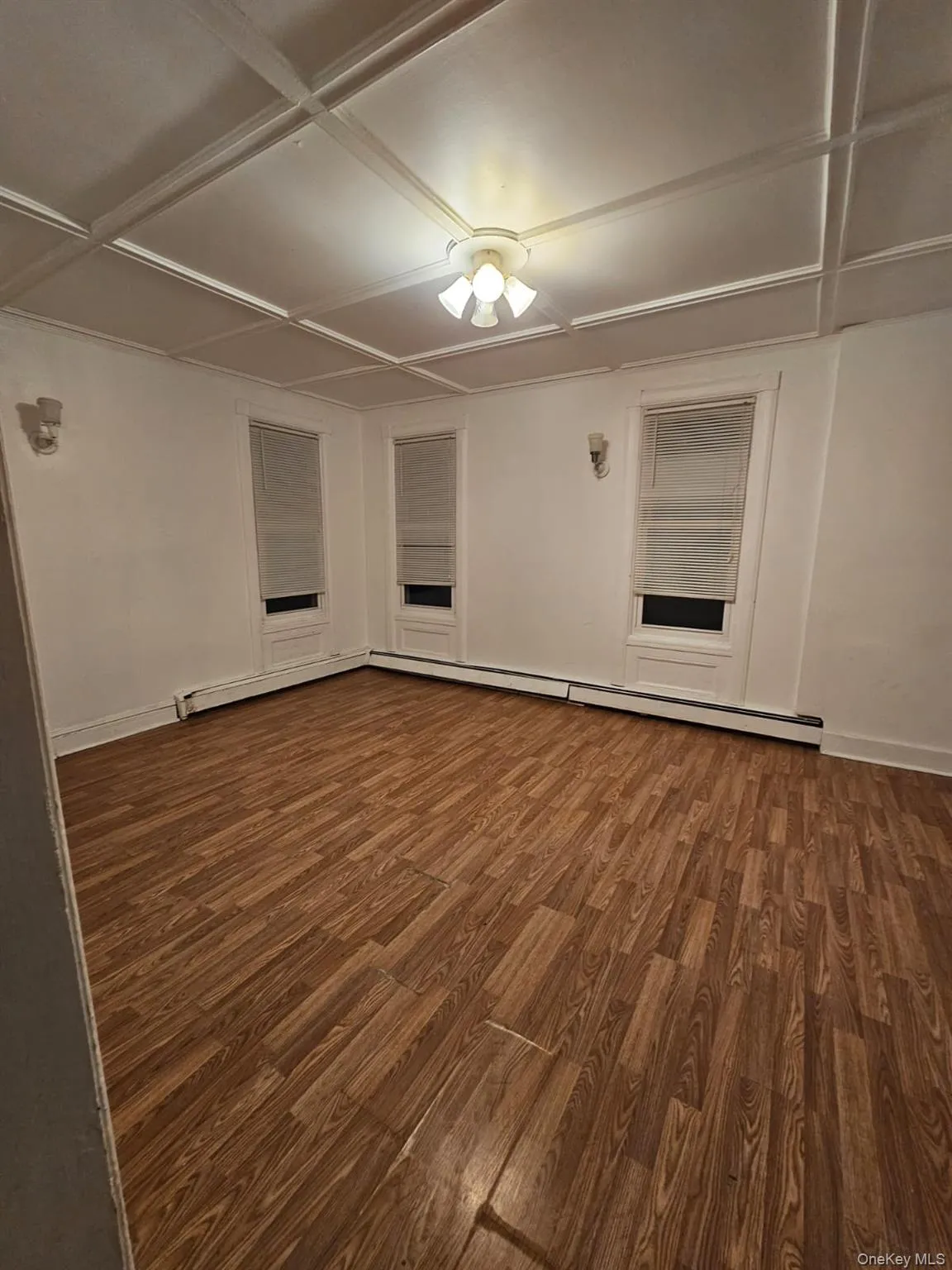Empty room with coffered ceiling, wood finished floors, and a baseboard heating unit Empty room with coffered ceiling, wood finished floors, and a baseboard heating unit