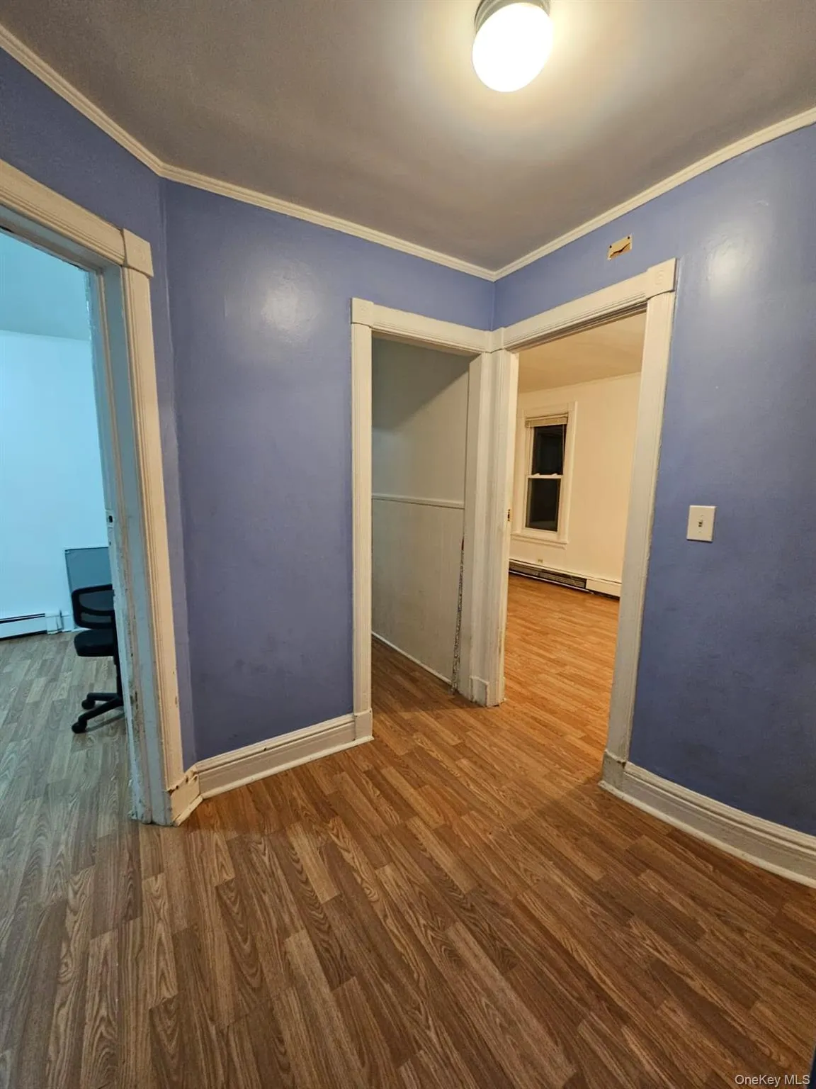 Empty room with ornamental molding, dark wood-style floors, and a baseboard radiator Empty room with ornamental molding, dark wood-style floors, and a baseboard radiator