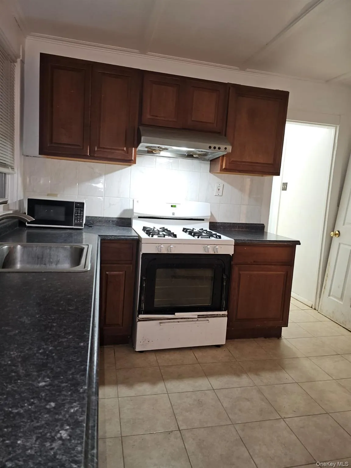 Kitchen with dark countertops, white range with gas stovetop, under cabinet range hood, and light tile patterned floors Kitchen with dark countertops, white range with gas stovetop, under cabinet range hood, and light tile patterned floors