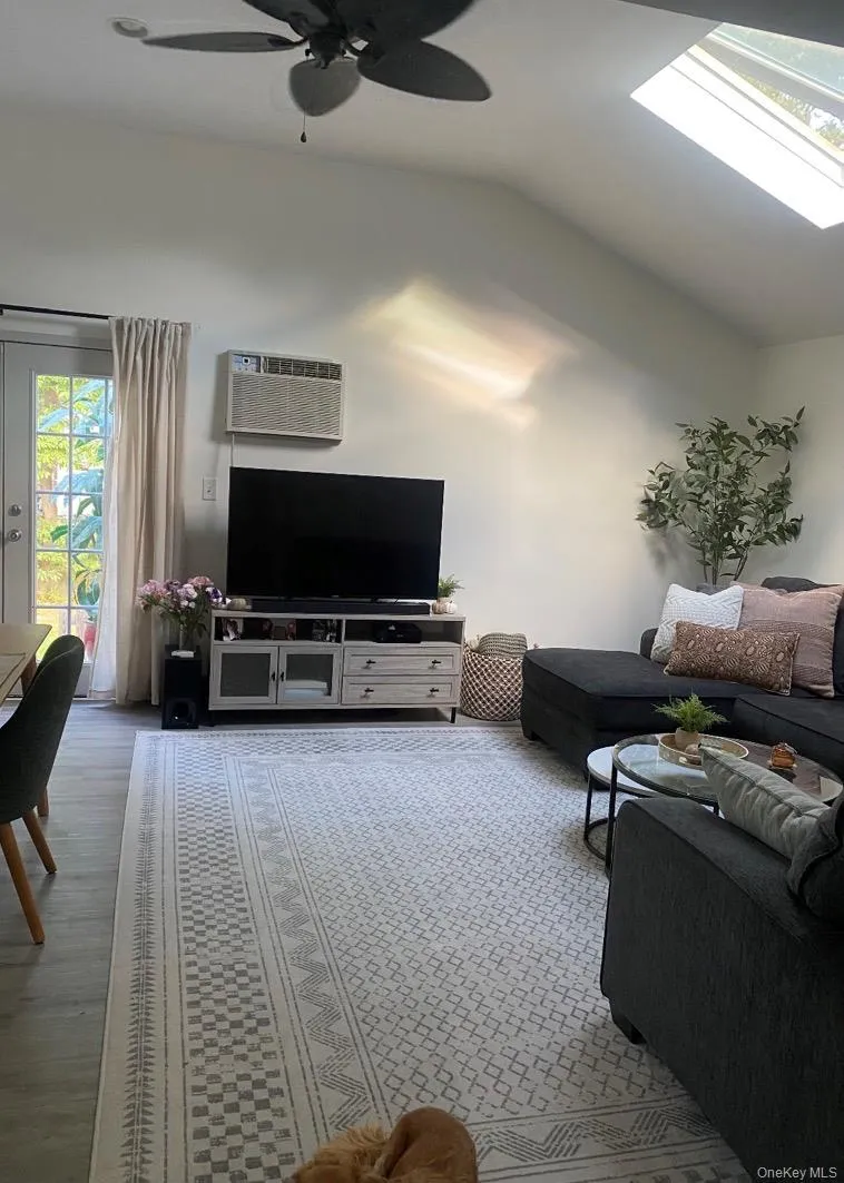 Living room featuring a skylight, vaulted ceiling, ceiling fan, and a wall mounted AC Living room featuring a skylight, vaulted ceiling, ceiling fan, and a wall mounted AC