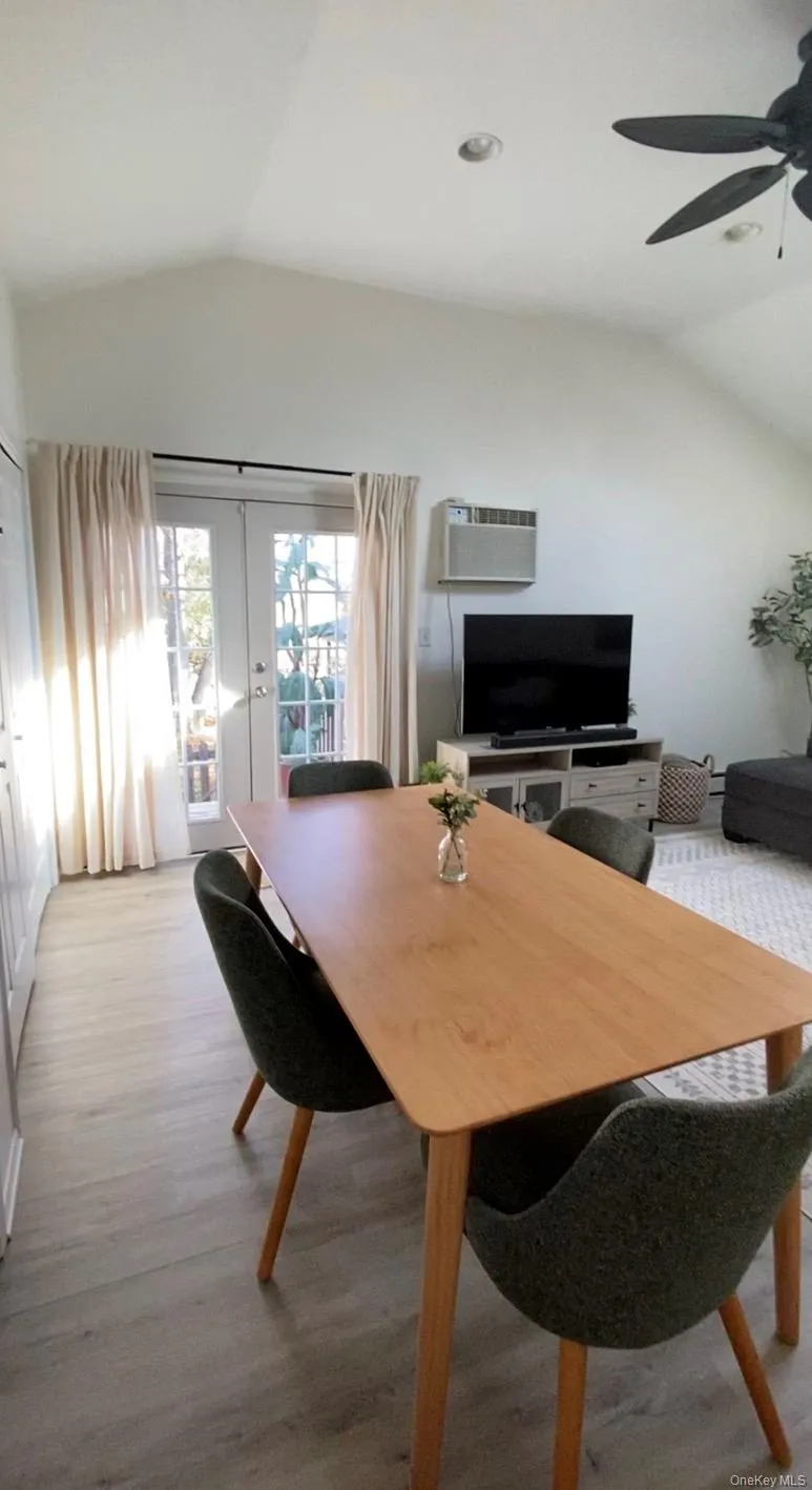 Dining area with lofted ceiling, french doors, light wood-style flooring, ceiling fan, and an AC wall unit Dining area with lofted ceiling, french doors, light wood-style flooring, ceiling fan, and an AC wall unit