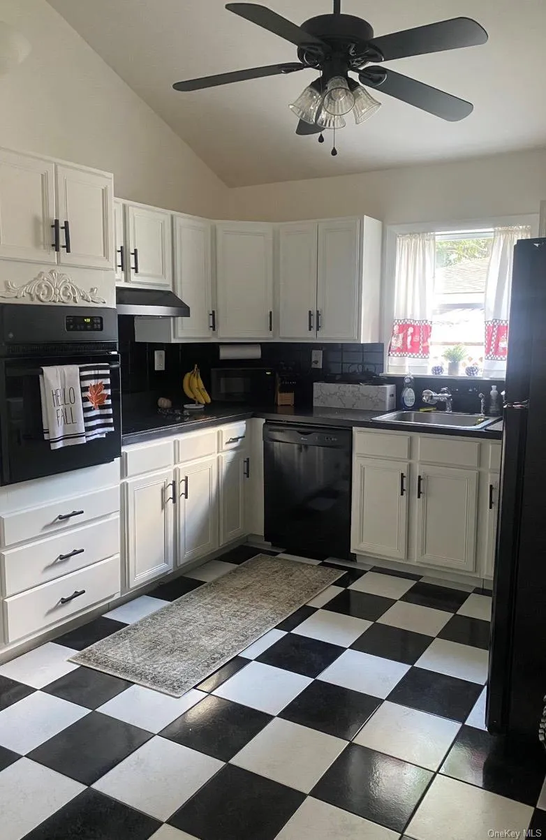 Kitchen with vaulted ceiling, white cabinetry, dark flooring, black appliances, and ceiling fan Kitchen with vaulted ceiling, white cabinetry, dark flooring, black appliances, and ceiling fan