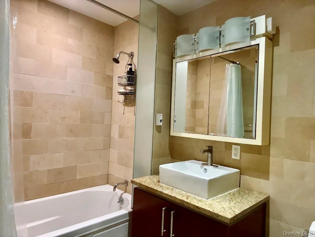 Bathroom featuring shower / tub combo with curtain, vanity, and tile walls Bathroom featuring shower / tub combo with curtain, vanity, and tile walls