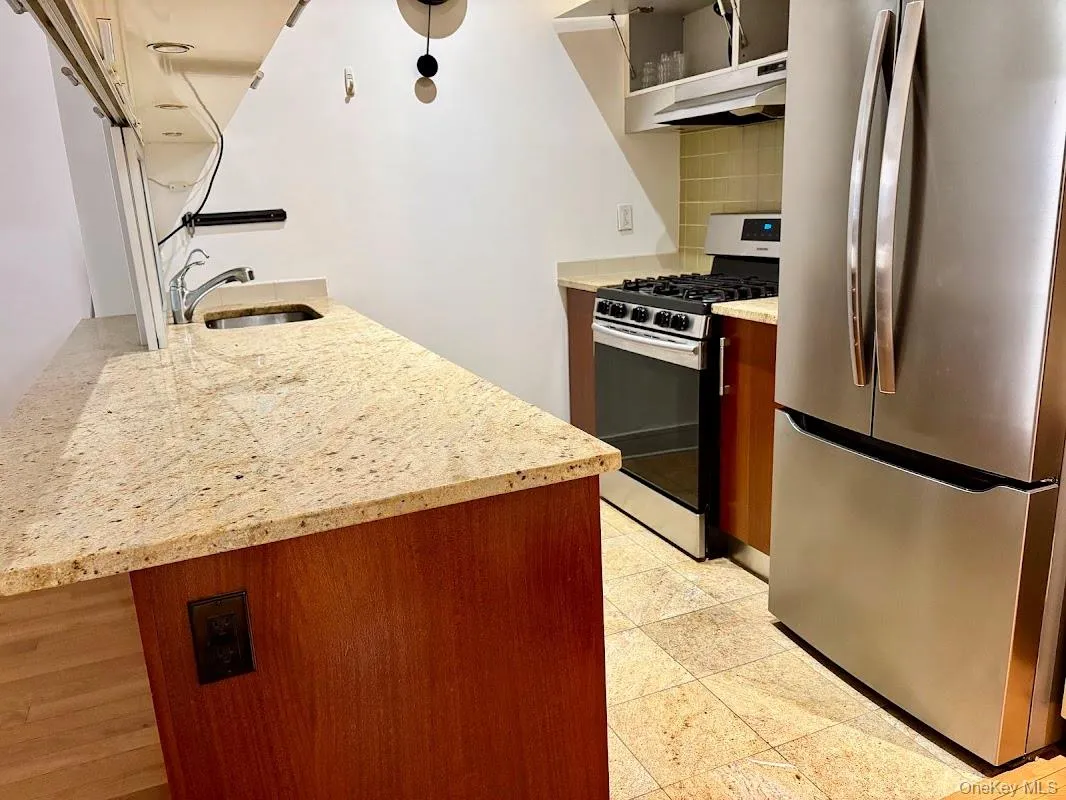 Kitchen featuring stainless steel appliances, open shelves, light stone countertops, under cabinet range hood, and tasteful backsplash Kitchen featuring stainless steel appliances, open shelves, light stone countertops, under cabinet range hood, and tasteful backsplash