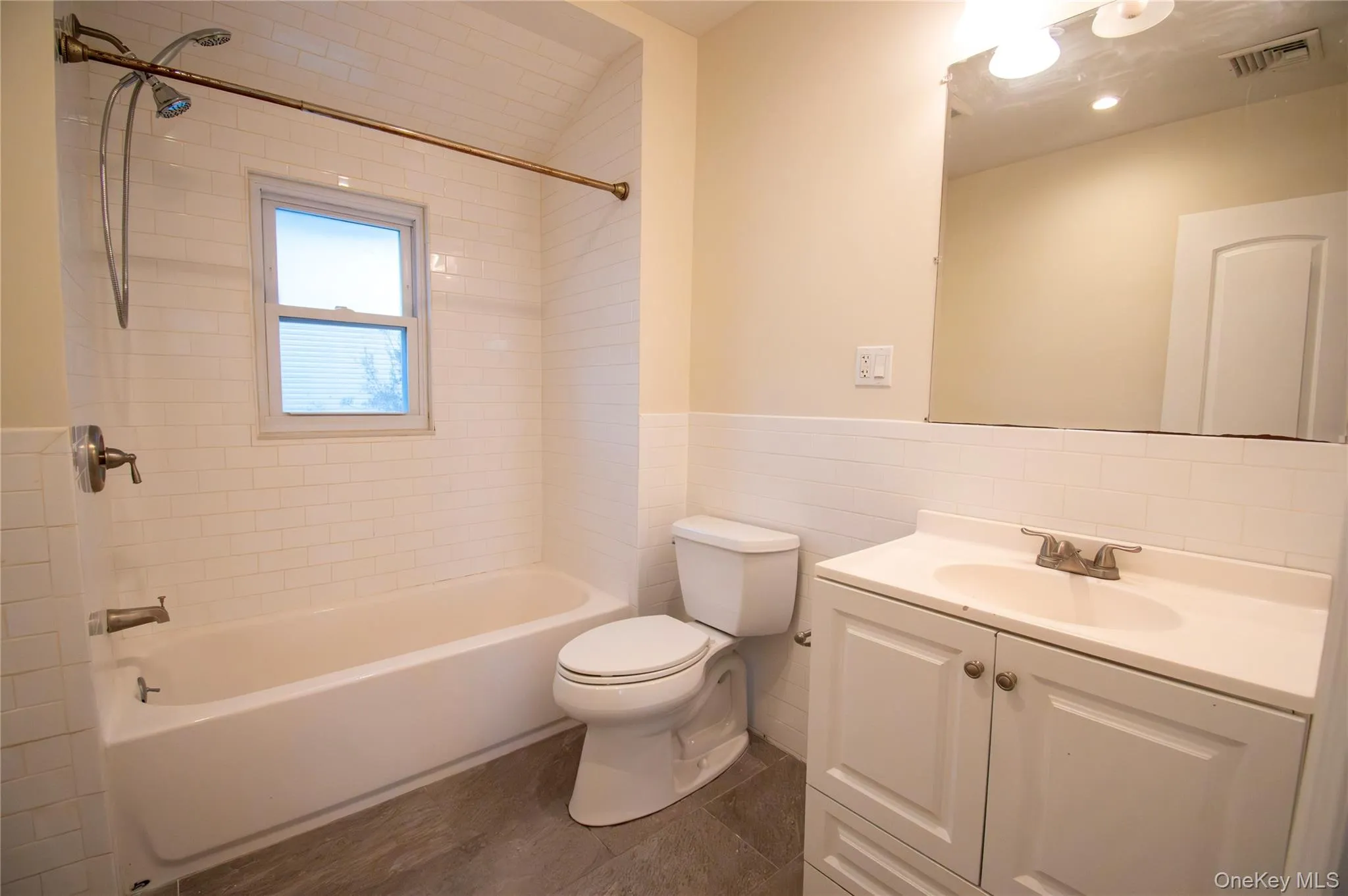 Bathroom featuring vanity, shower / bathtub combination, tile walls, and a wainscoted wall Bathroom featuring vanity, shower / bathtub combination, tile walls, and a wainscoted wall