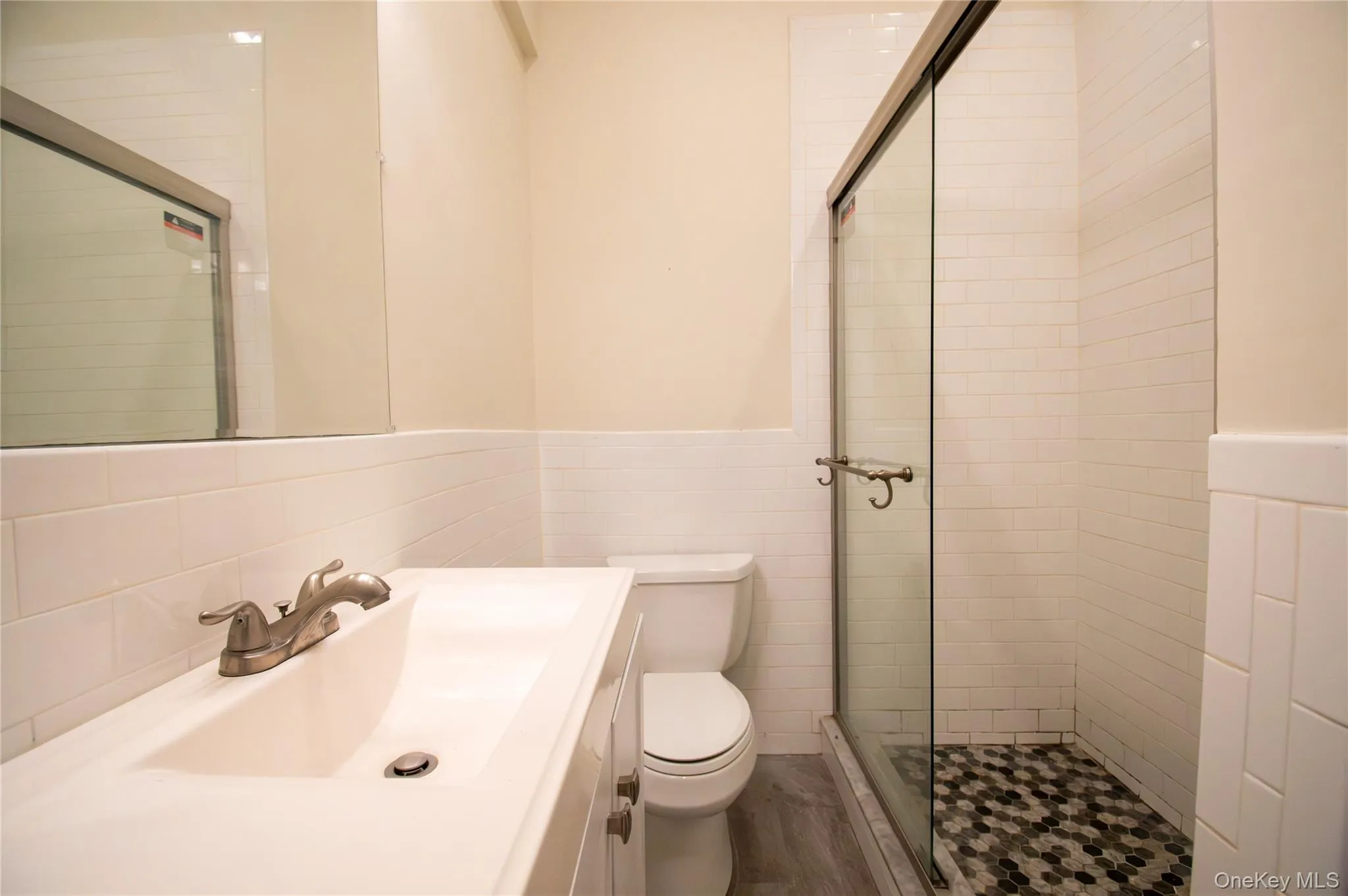Bathroom featuring a stall shower, vanity, wainscoting, and tile walls Bathroom featuring a stall shower, vanity, wainscoting, and tile walls