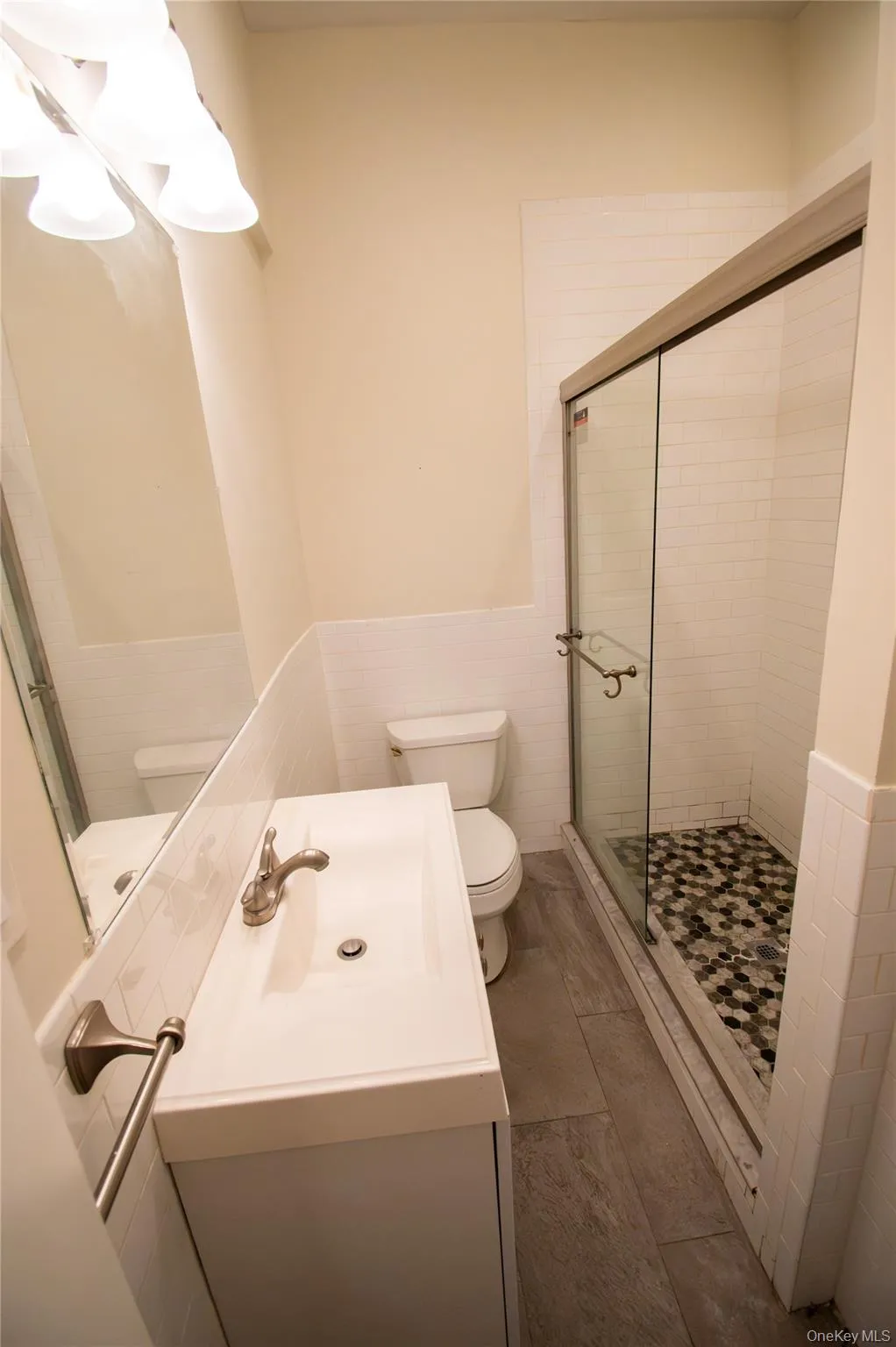 Bathroom featuring wainscoting, a shower stall, vanity, and tile walls Bathroom featuring wainscoting, a shower stall, vanity, and tile walls