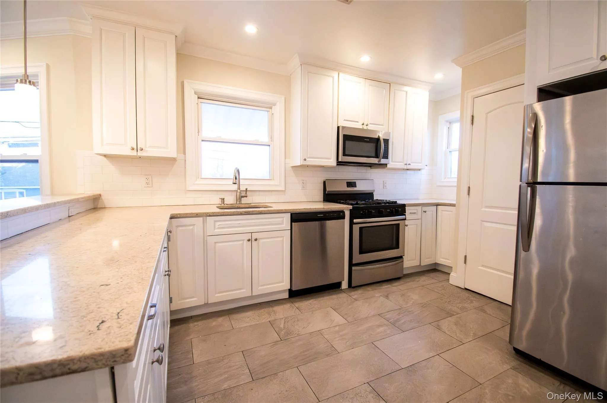 Kitchen with stainless steel appliances, white cabinets, ornamental molding, light stone counters, and decorative light fixtures Kitchen with stainless steel appliances, white cabinets, ornamental molding, light stone counters, and decorative light fixtures