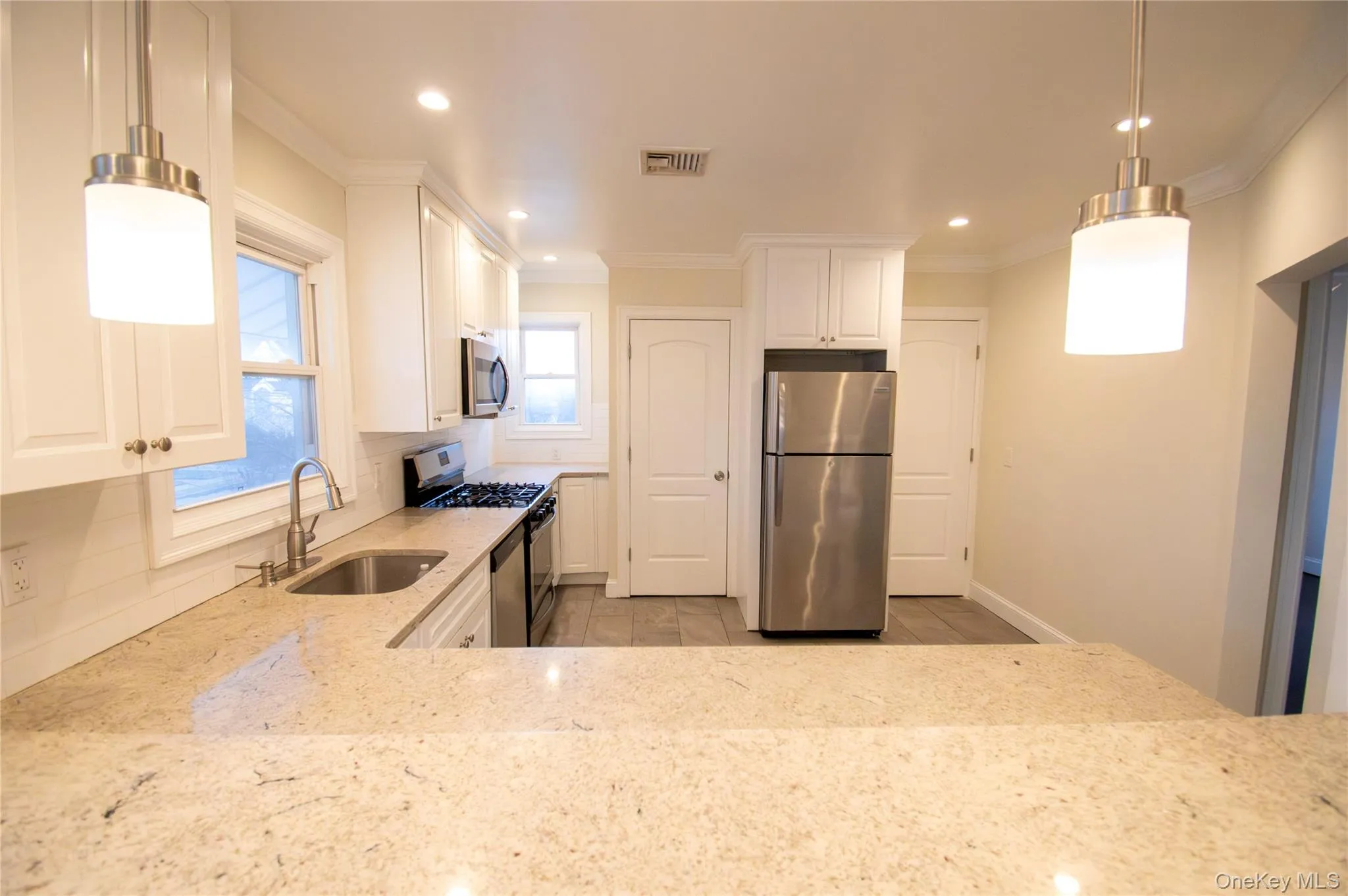 Kitchen with decorative light fixtures, light stone countertops, white cabinets, stainless steel appliances, and decorative backsplash Kitchen with decorative light fixtures, light stone countertops, white cabinets, stainless steel appliances, and decorative backsplash
