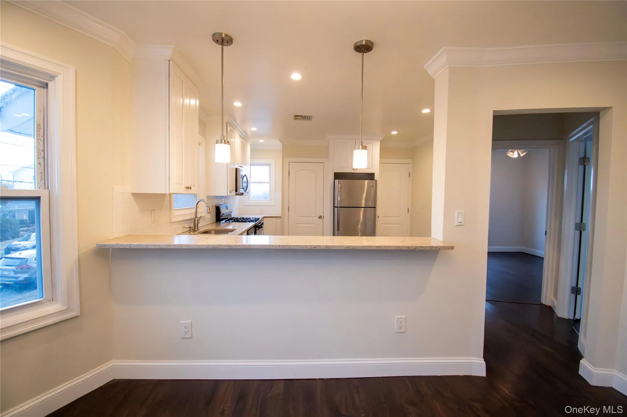 Kitchen featuring light stone counters, stainless steel appliances, white cabinetry, decorative light fixtures, and dark wood-type flooring Kitchen featuring light stone counters, stainless steel appliances, white cabinetry, decorative light fixtures, and dark wood-type flooring
