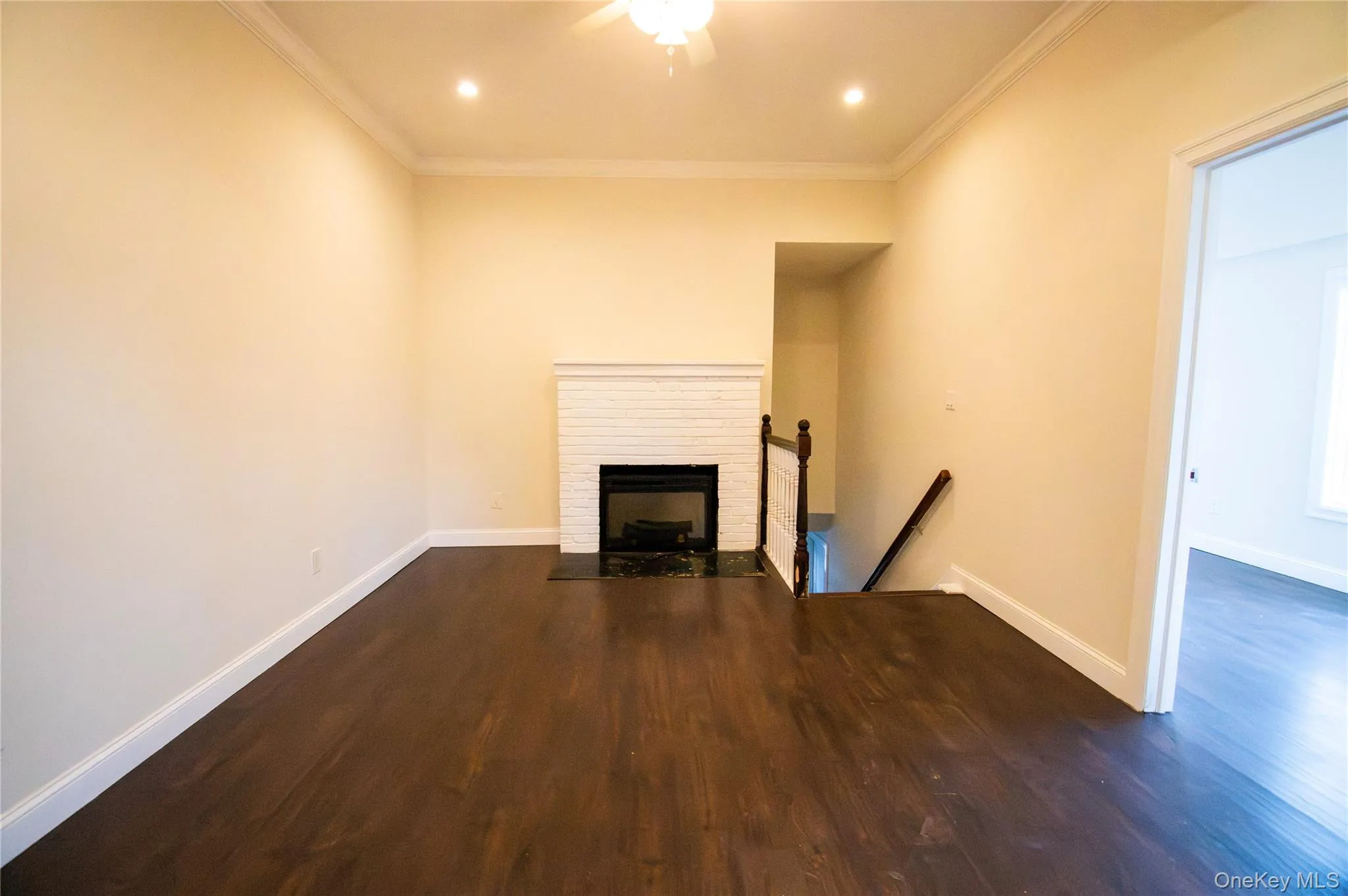 Unfurnished living room with a brick fireplace, dark wood-type flooring, ornamental molding, recessed lighting, and ceiling fan Unfurnished living room with a brick fireplace, dark wood-type flooring, ornamental molding, recessed lighting, and ceiling fan