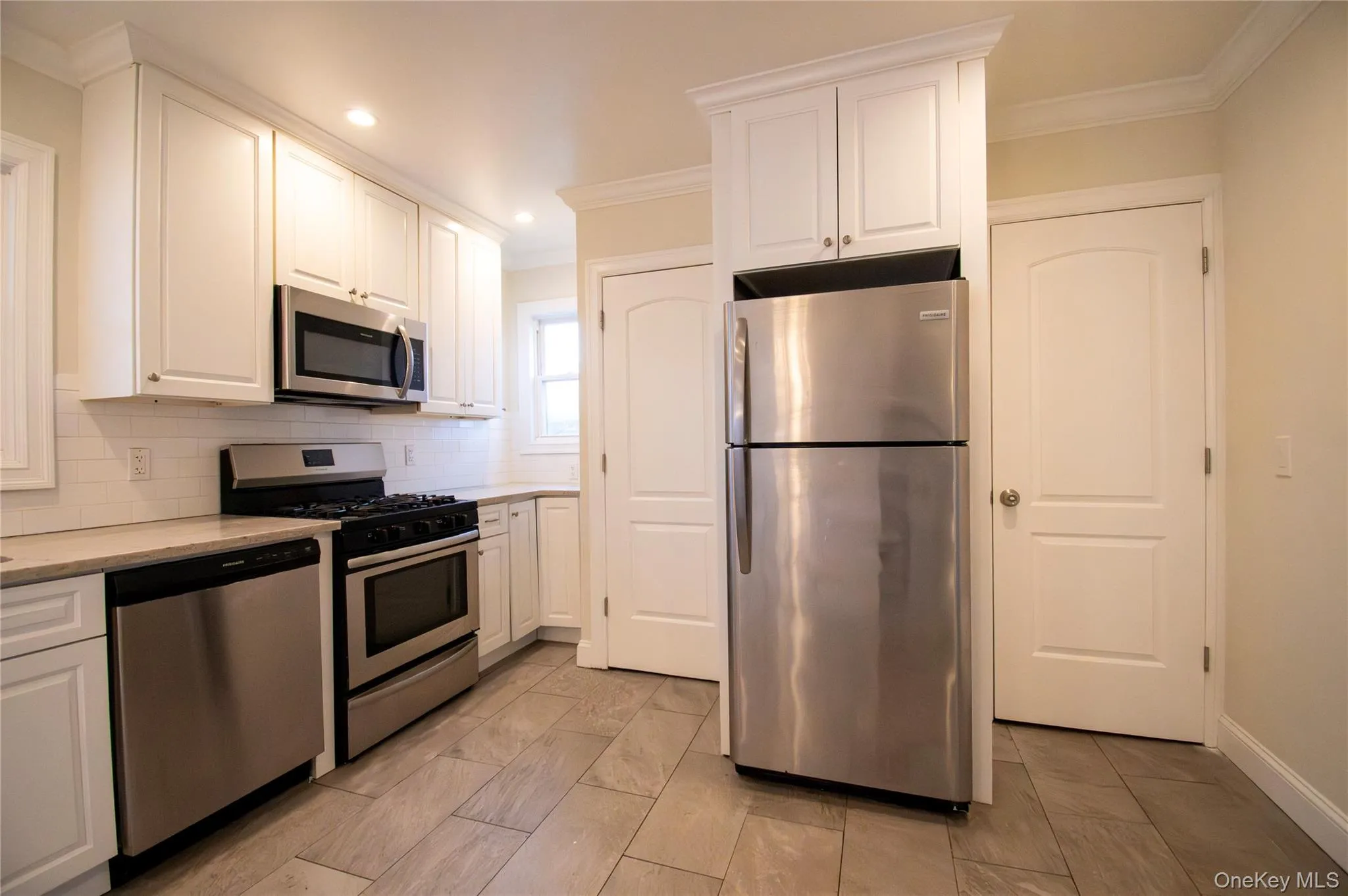 Kitchen with appliances with stainless steel finishes, white cabinets, ornamental molding, backsplash, and light stone counters Kitchen with appliances with stainless steel finishes, white cabinets, ornamental molding, backsplash, and light stone counters