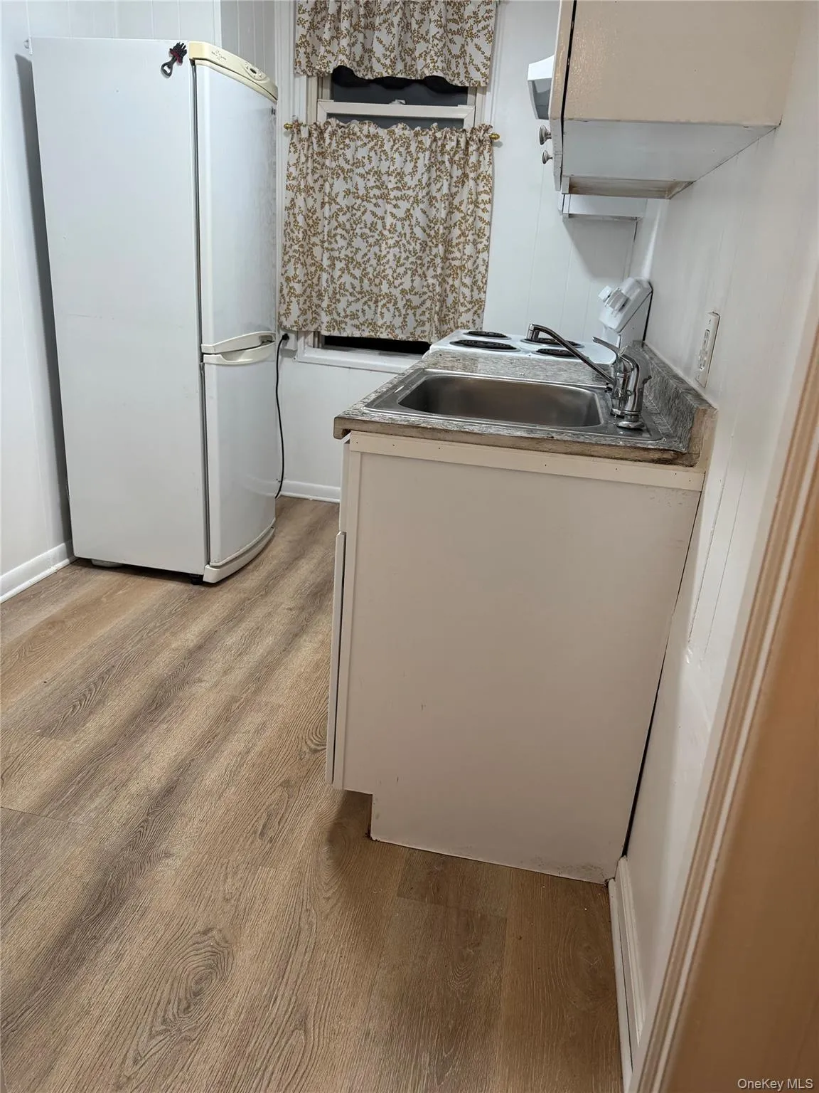 Kitchen with freestanding refrigerator, light wood-style floors, white cabinets, and stove Kitchen with freestanding refrigerator, light wood-style floors, white cabinets, and stove