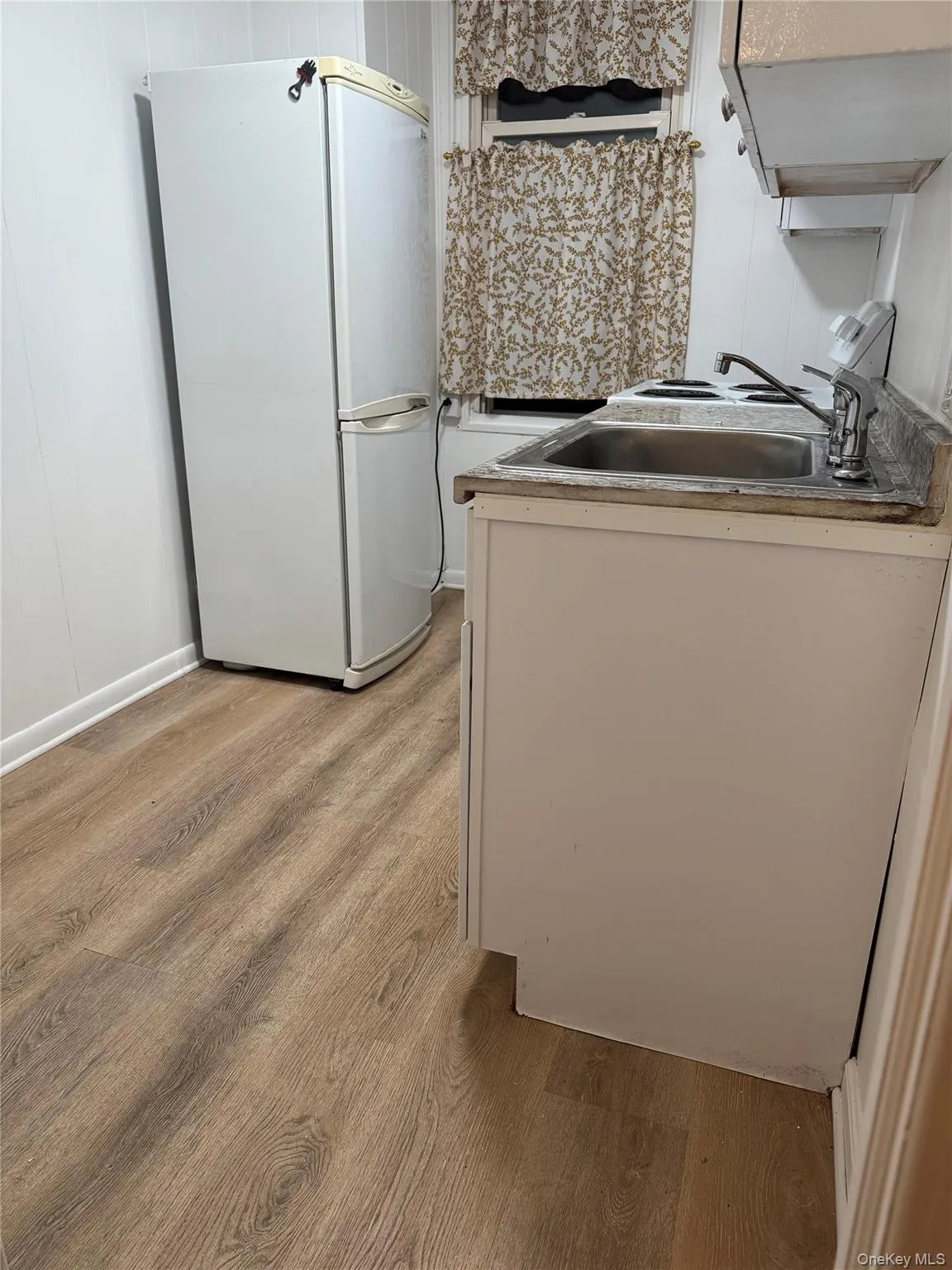Kitchen with freestanding refrigerator, light wood-style floors, white cabinetry, and extractor fan Kitchen with freestanding refrigerator, light wood-style floors, white cabinetry, and extractor fan