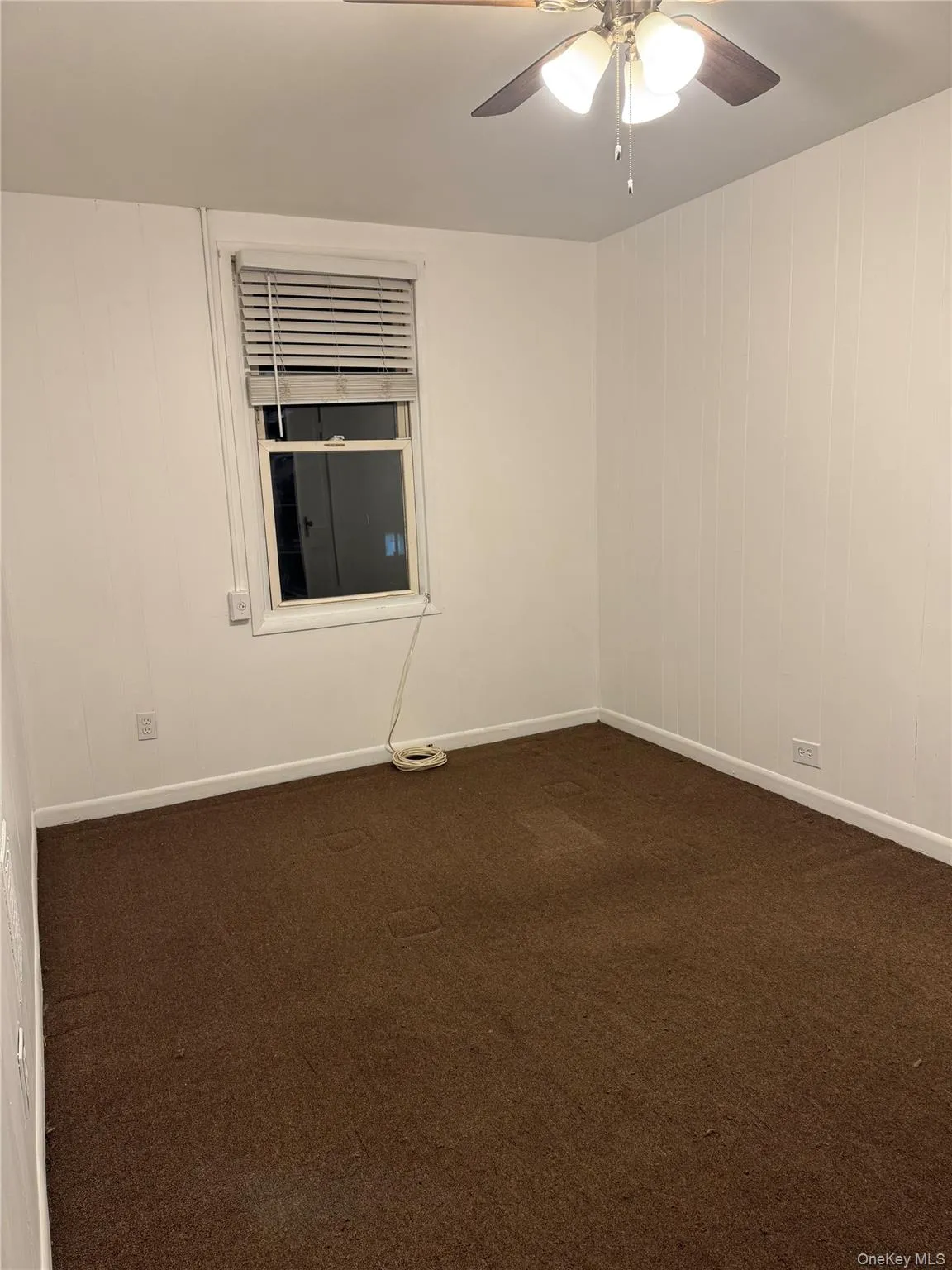 Empty room with dark carpet, wooden walls, and a ceiling fan Empty room with dark carpet, wooden walls, and a ceiling fan