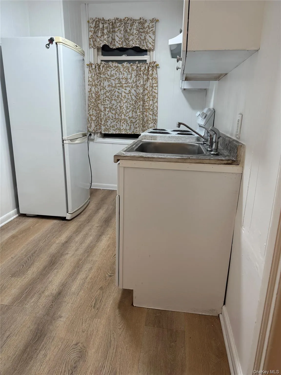 Kitchen with freestanding refrigerator, light wood-type flooring, and white cabinets Kitchen with freestanding refrigerator, light wood-type flooring, and white cabinets