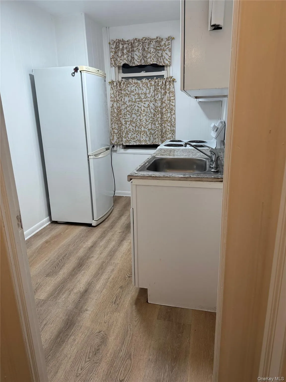 Kitchen featuring white appliances, white cabinetry, light wood-style floors, and light countertops Kitchen featuring white appliances, white cabinetry, light wood-style floors, and light countertops