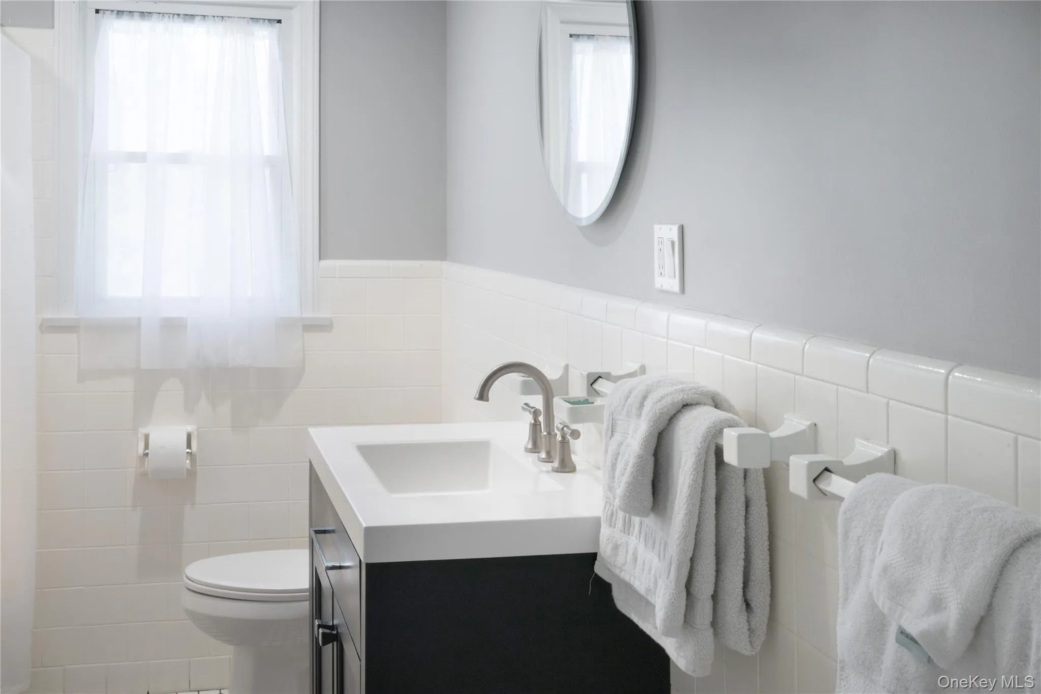 Bathroom with vanity, a wainscoted wall, tile walls, and healthy amount of natural light Bathroom with vanity, a wainscoted wall, tile walls, and healthy amount of natural light