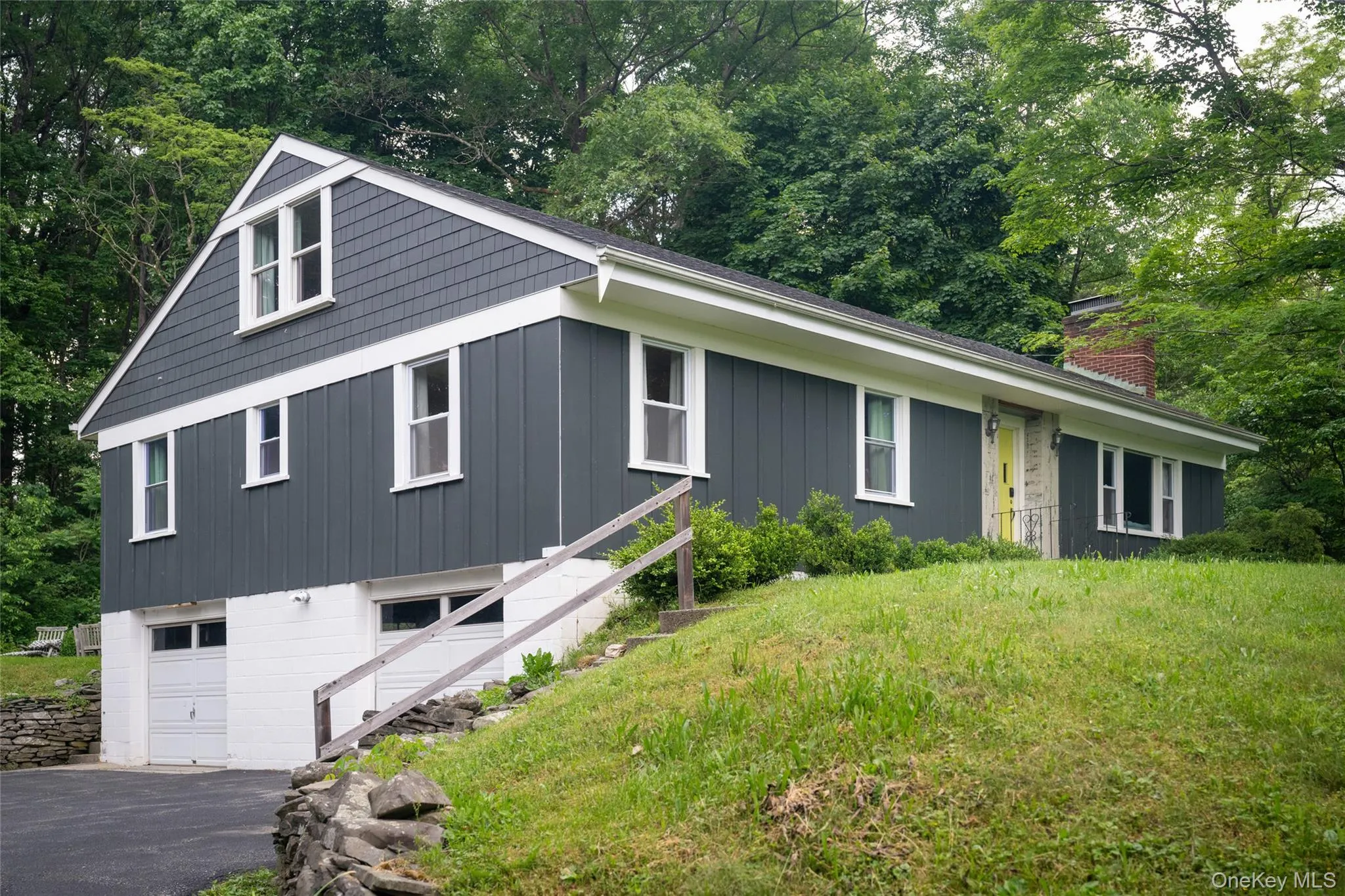 View of front of home featuring board and batten siding, view of scattered trees, an attached garage, a chimney, and asphalt driveway View of front of home featuring board and batten siding, view of scattered trees, an attached garage, a chimney, and asphalt driveway