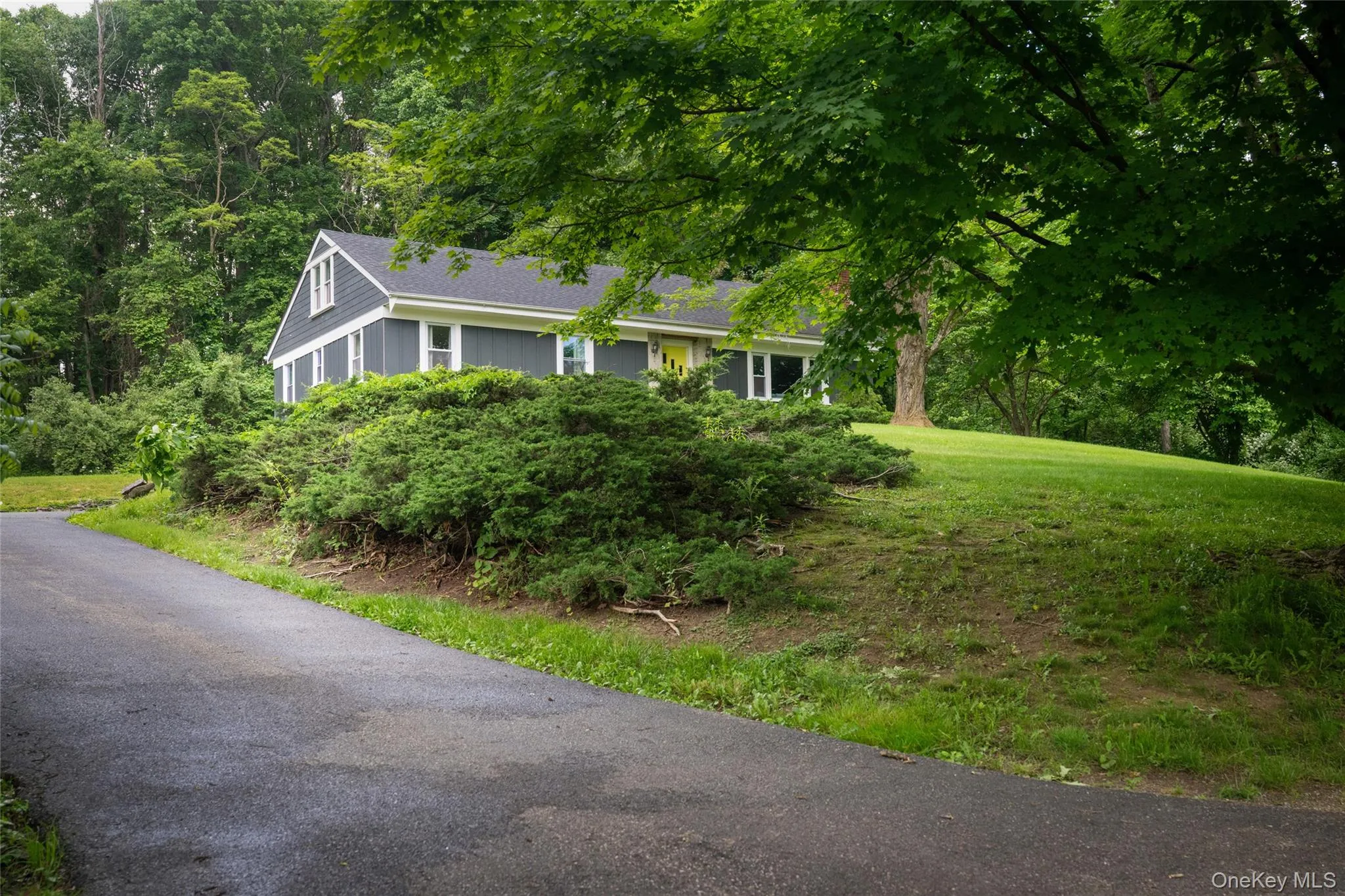 Ranch-style home featuring a front lawn, roof with shingles, and view of wooded area Ranch-style home featuring a front lawn, roof with shingles, and view of wooded area