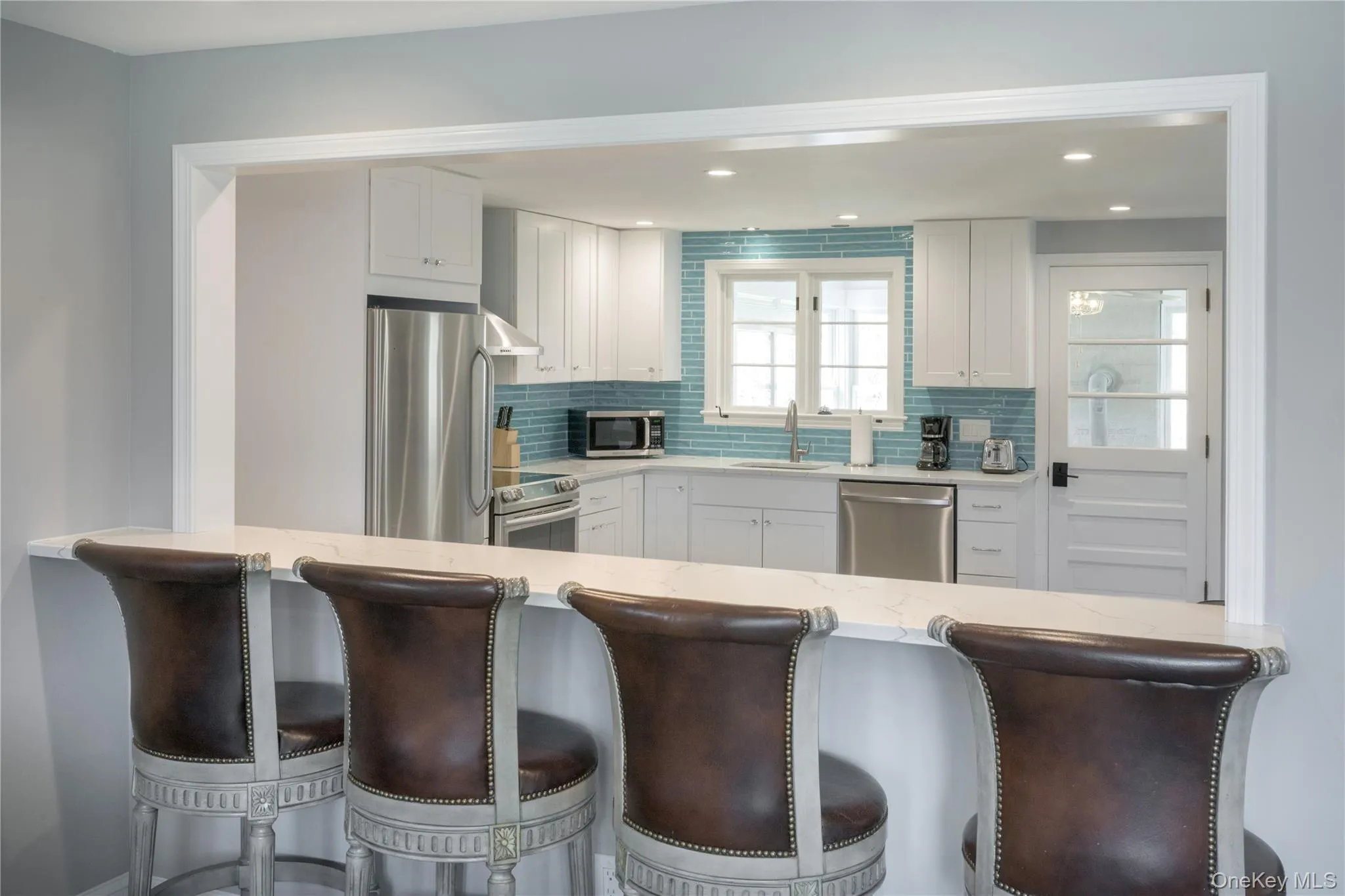 Kitchen with a kitchen breakfast bar, white cabinetry, appliances with stainless steel finishes, tasteful backsplash, and recessed lighting Kitchen with a kitchen breakfast bar, white cabinetry, appliances with stainless steel finishes, tasteful backsplash, and recessed lighting