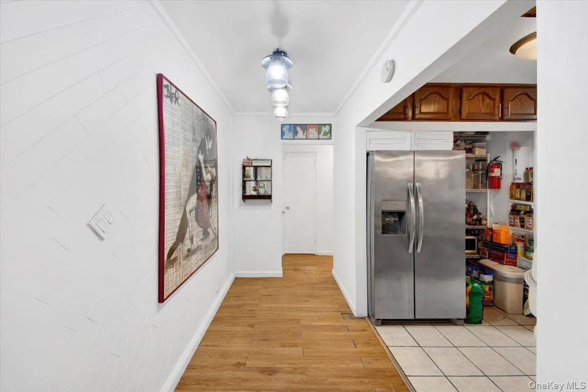 Kitchen featuring light wood-style floors, stainless steel refrigerator with ice dispenser, ornamental molding, and brown cabinetry Kitchen featuring light wood-style floors, stainless steel refrigerator with ice dispenser, ornamental molding, and brown cabinetry
