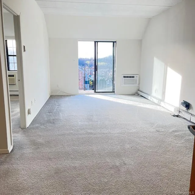 Empty room with carpet, lofted ceiling, a wall mounted air conditioner, and baseboard heating Empty room with carpet, lofted ceiling, a wall mounted air conditioner, and baseboard heating