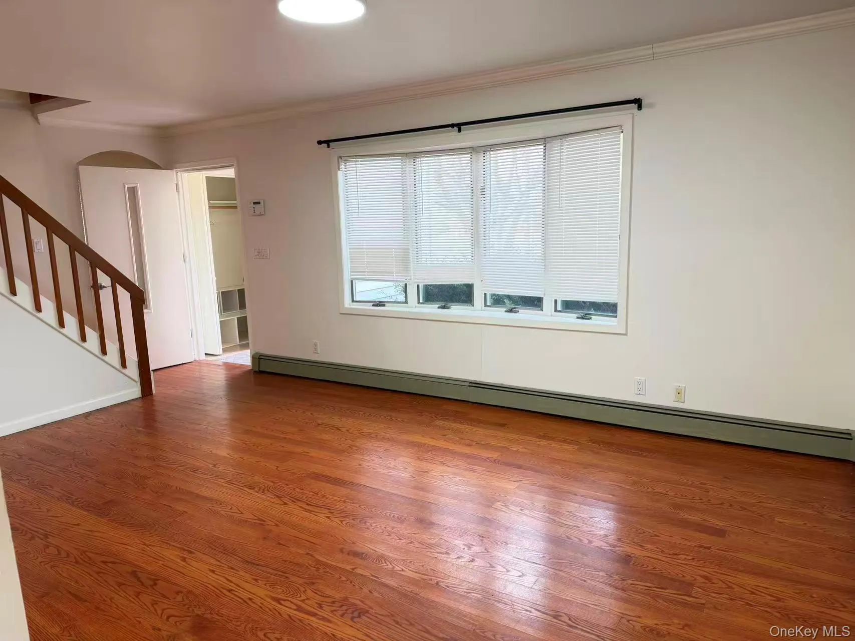 Unfurnished living room featuring stairs, baseboard heating, wood finished floors, and crown molding Unfurnished living room featuring stairs, baseboard heating, wood finished floors, and crown molding