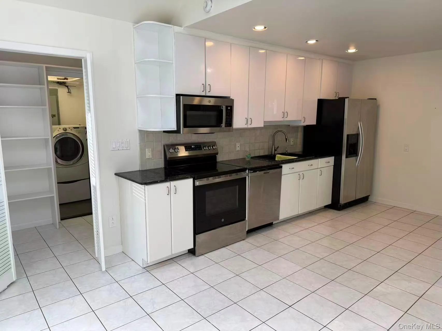 Kitchen with appliances with stainless steel finishes, white cabinets, open shelves, tasteful backsplash, and light tile patterned floors Kitchen with appliances with stainless steel finishes, white cabinets, open shelves, tasteful backsplash, and light tile patterned floors
