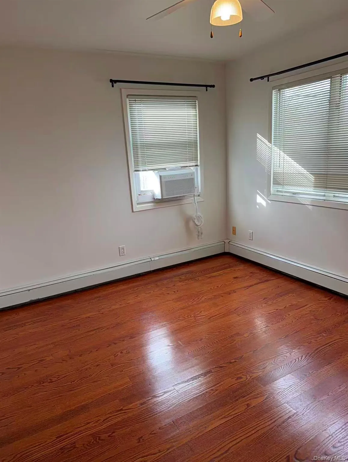 Unfurnished room featuring dark wood-style flooring, baseboard heating, ceiling fan, and cooling unit Unfurnished room featuring dark wood-style flooring, baseboard heating, ceiling fan, and cooling unit