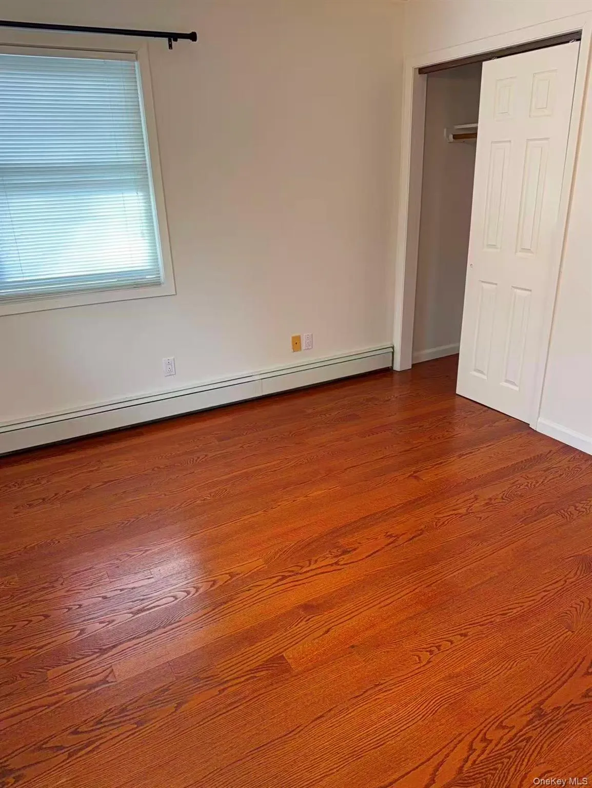 Unfurnished bedroom with a baseboard radiator, a closet, and dark wood-style flooring Unfurnished bedroom with a baseboard radiator, a closet, and dark wood-style flooring
