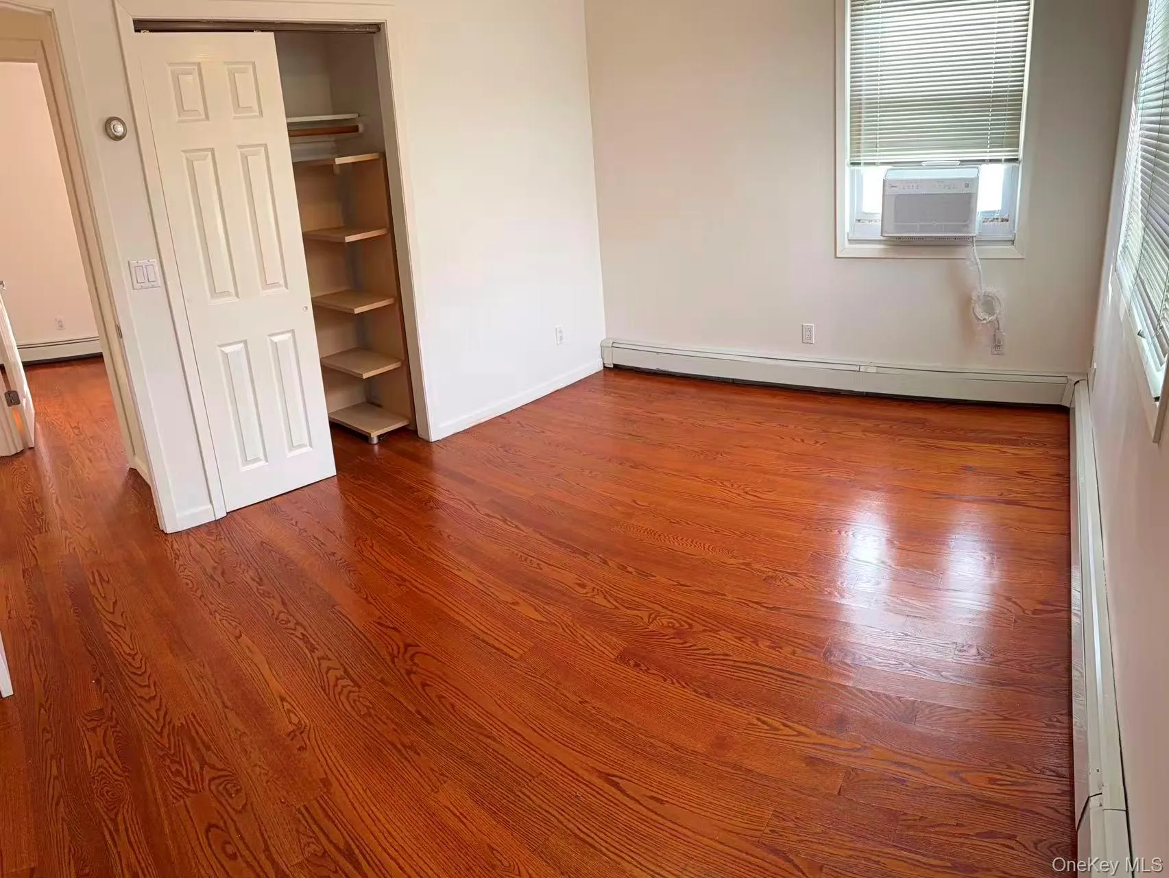 Unfurnished bedroom featuring dark wood-style flooring, a closet, a baseboard radiator, and cooling unit Unfurnished bedroom featuring dark wood-style flooring, a closet, a baseboard radiator, and cooling unit