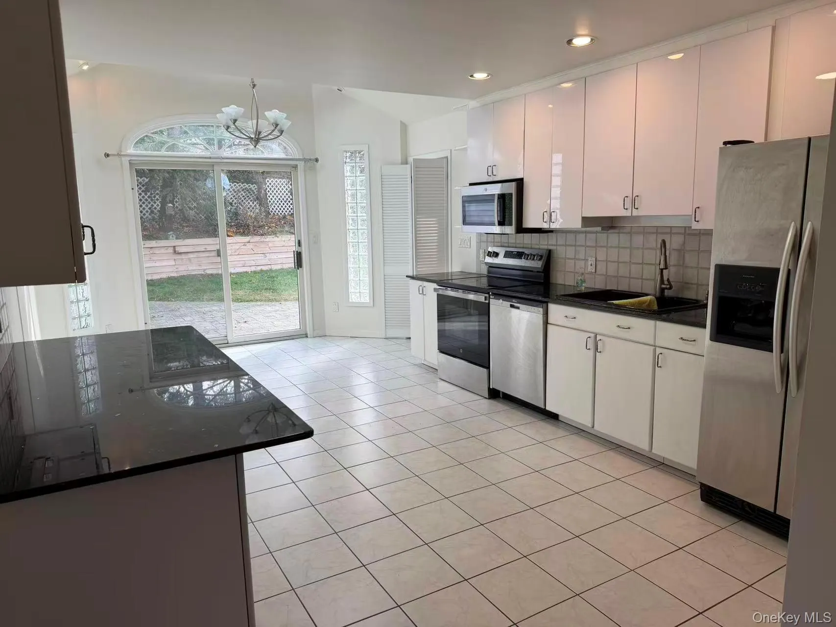 Kitchen featuring appliances with stainless steel finishes, white cabinetry, backsplash, light tile patterned floors, and a chandelier Kitchen featuring appliances with stainless steel finishes, white cabinetry, backsplash, light tile patterned floors, and a chandelier