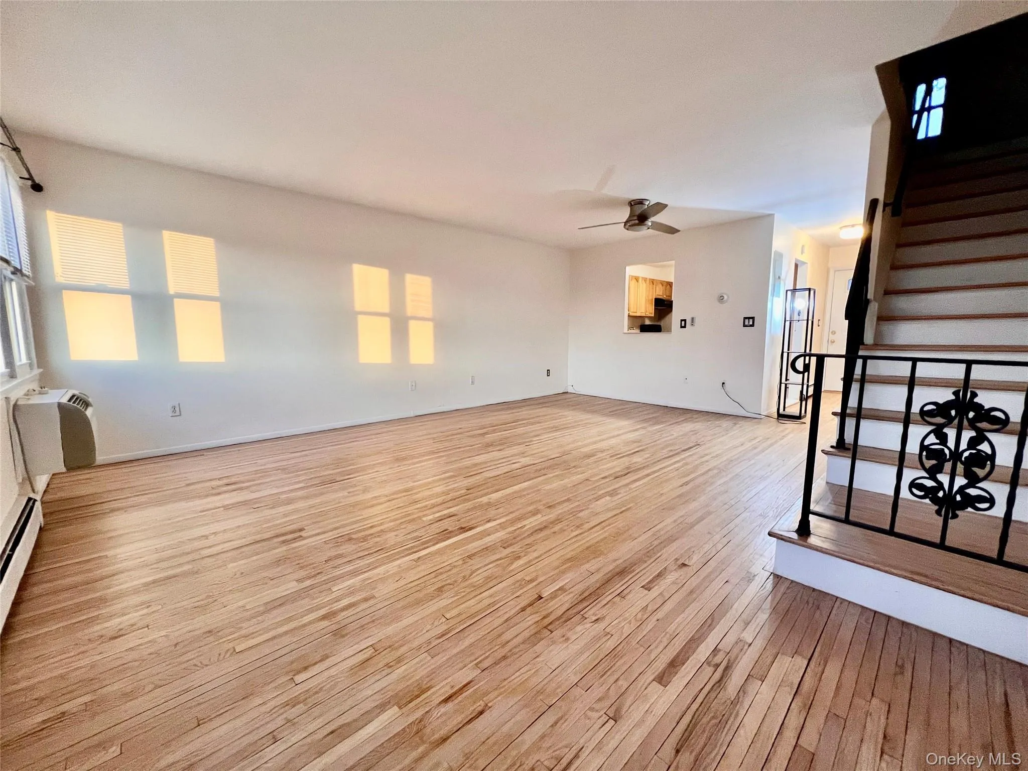 Unfurnished living room with stairway, light wood-style floors, ceiling fan, and a wall mounted AC Unfurnished living room with stairway, light wood-style floors, ceiling fan, and a wall mounted AC