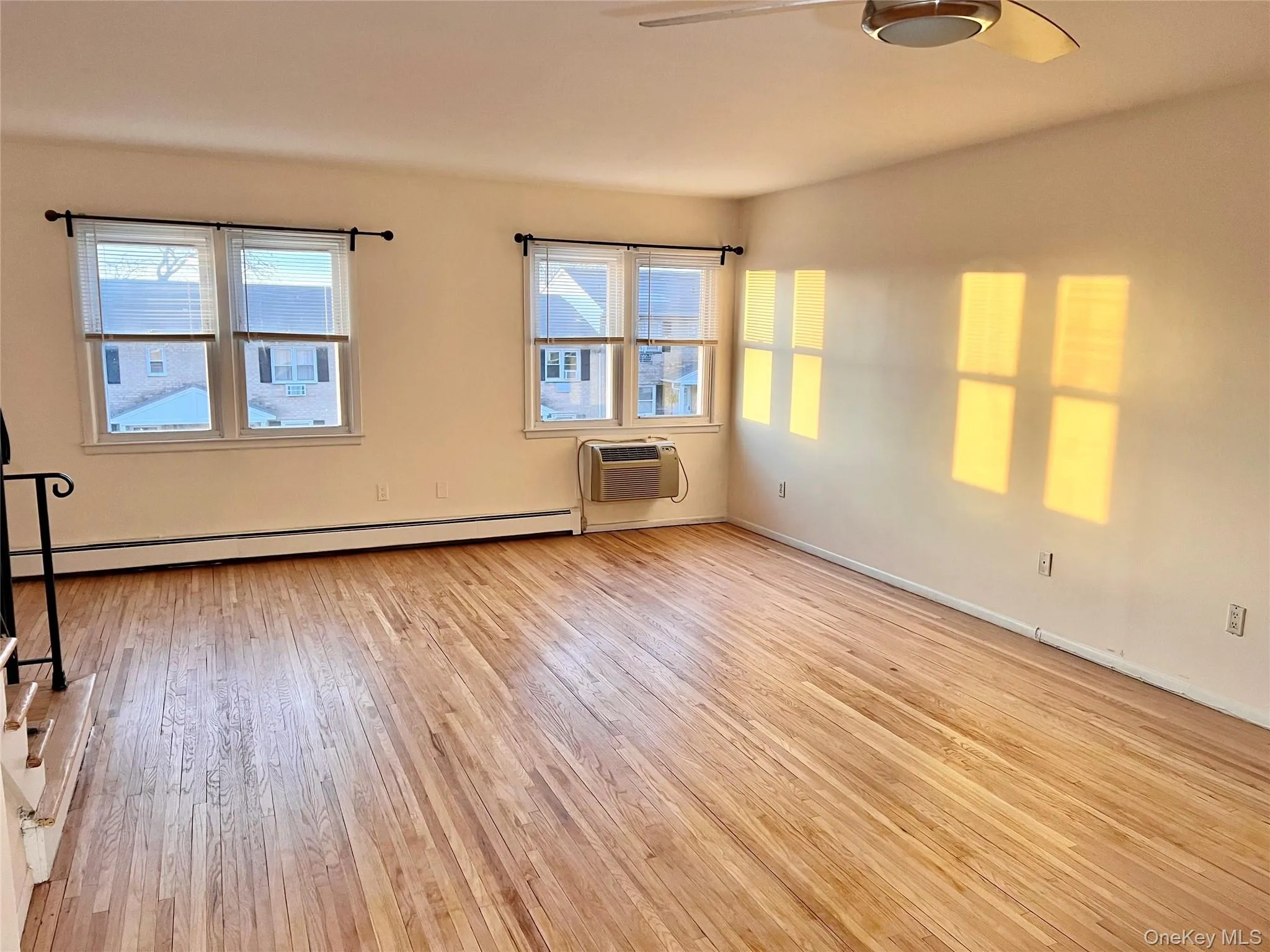 Spare room with light wood-style flooring, a baseboard heating unit, ceiling fan, and an AC wall unit Spare room with light wood-style flooring, a baseboard heating unit, ceiling fan, and an AC wall unit