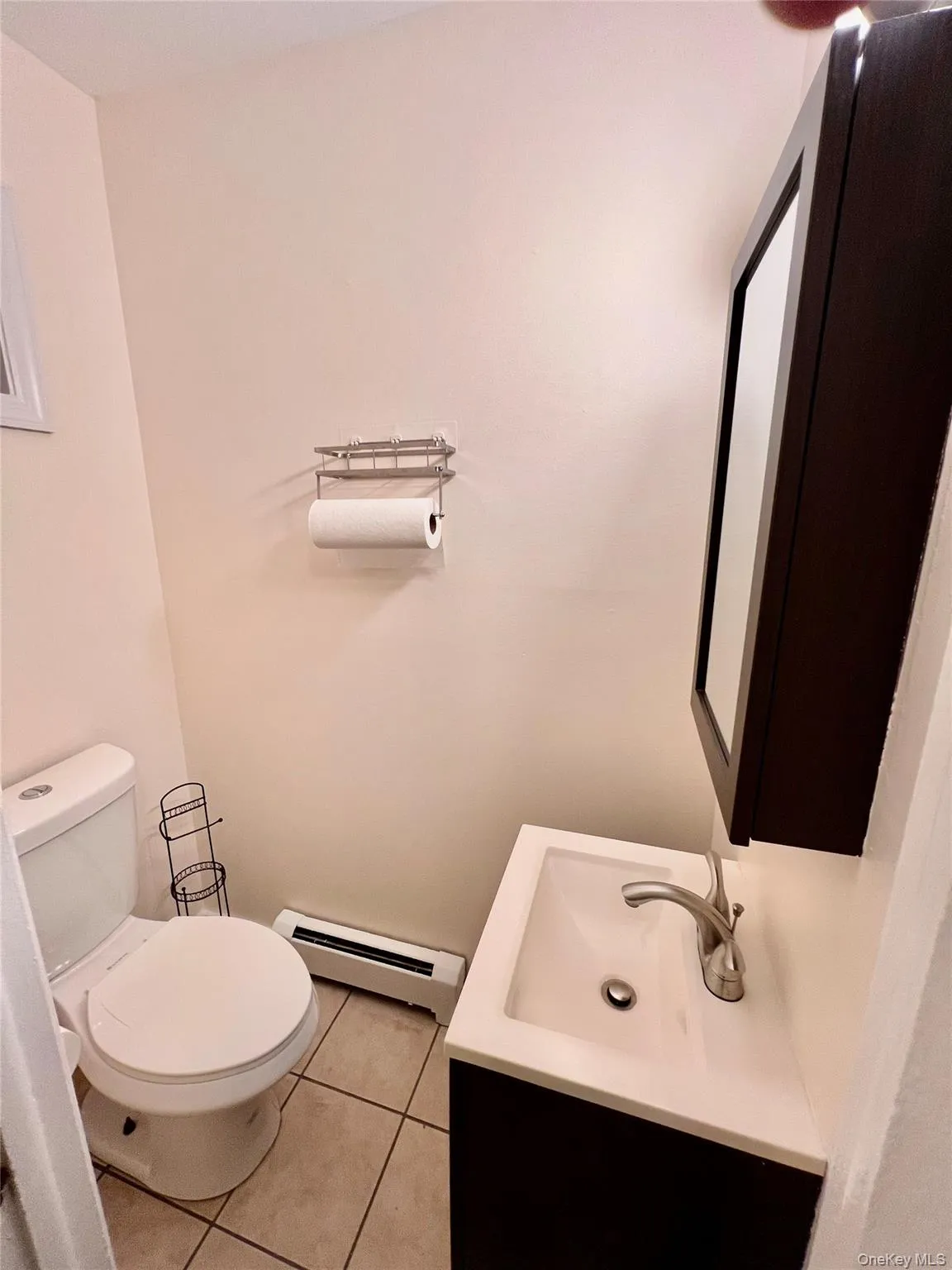 Half bathroom featuring a baseboard heating unit, vanity, and light tile patterned floors Half bathroom featuring a baseboard heating unit, vanity, and light tile patterned floors