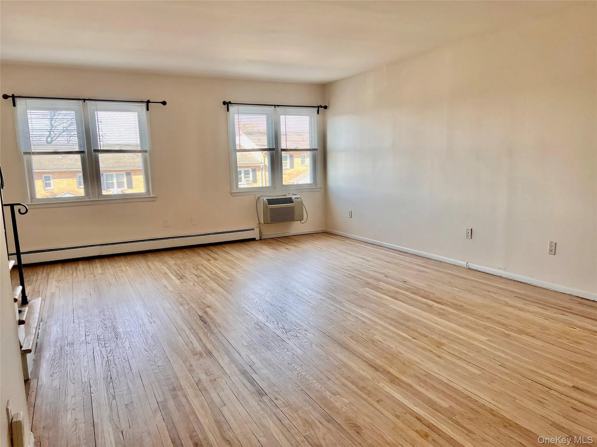 Unfurnished room featuring a baseboard radiator, light wood-type flooring, and a wall mounted air conditioner Unfurnished room featuring a baseboard radiator, light wood-type flooring, and a wall mounted air conditioner