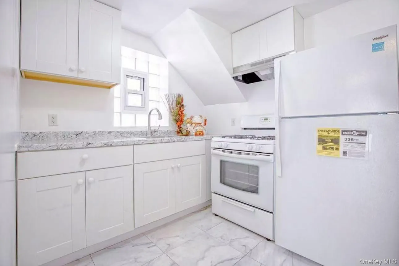Kitchen with white appliances, white cabinets, light marble finish floors, light stone counters, and under cabinet range hood Kitchen with white appliances, white cabinets, light marble finish floors, light stone counters, and under cabinet range hood