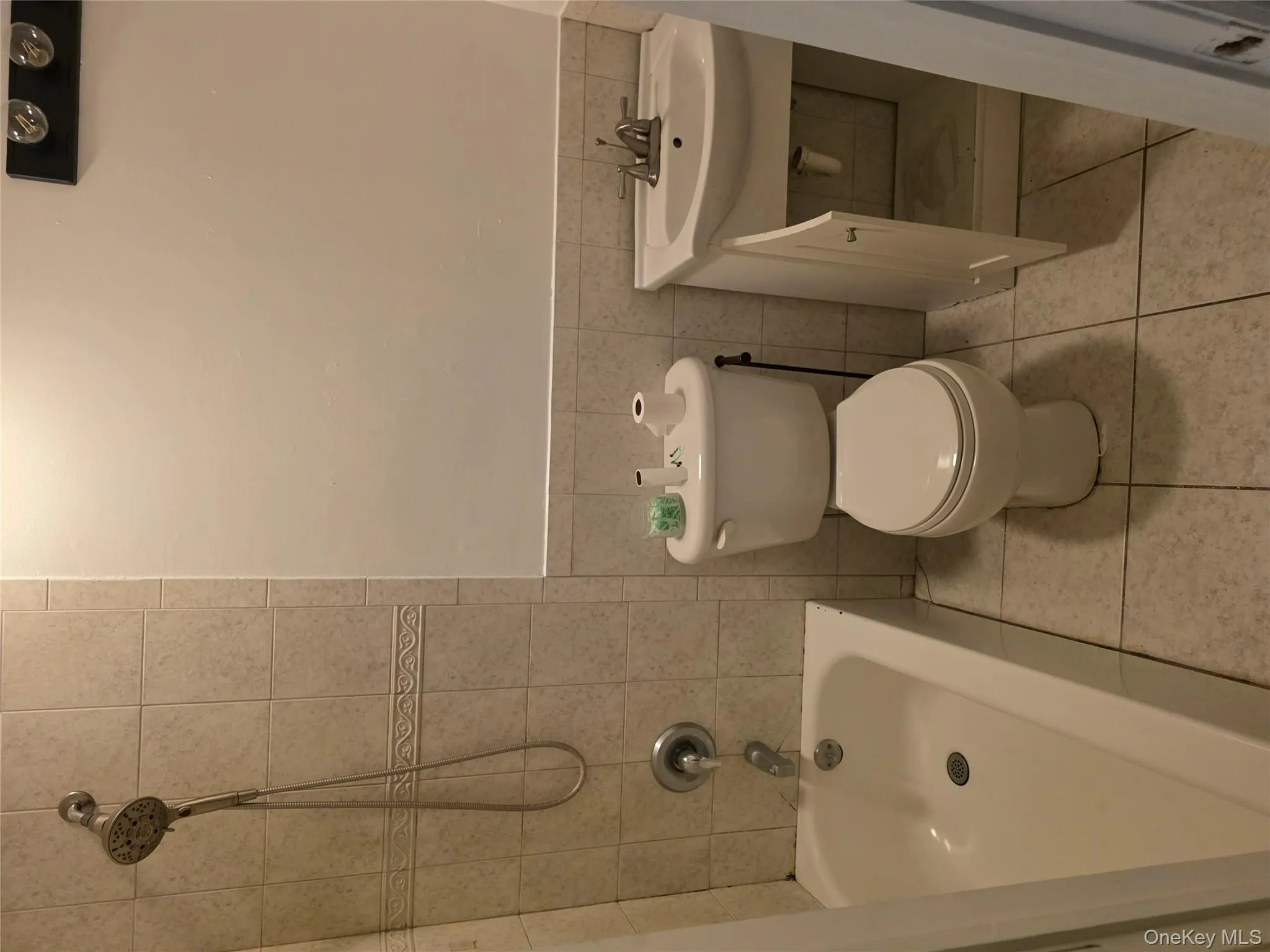 Bathroom featuring tile walls, vanity, shower / washtub combination, wainscoting, and light tile patterned floors Bathroom featuring tile walls, vanity, shower / washtub combination, wainscoting, and light tile patterned floors