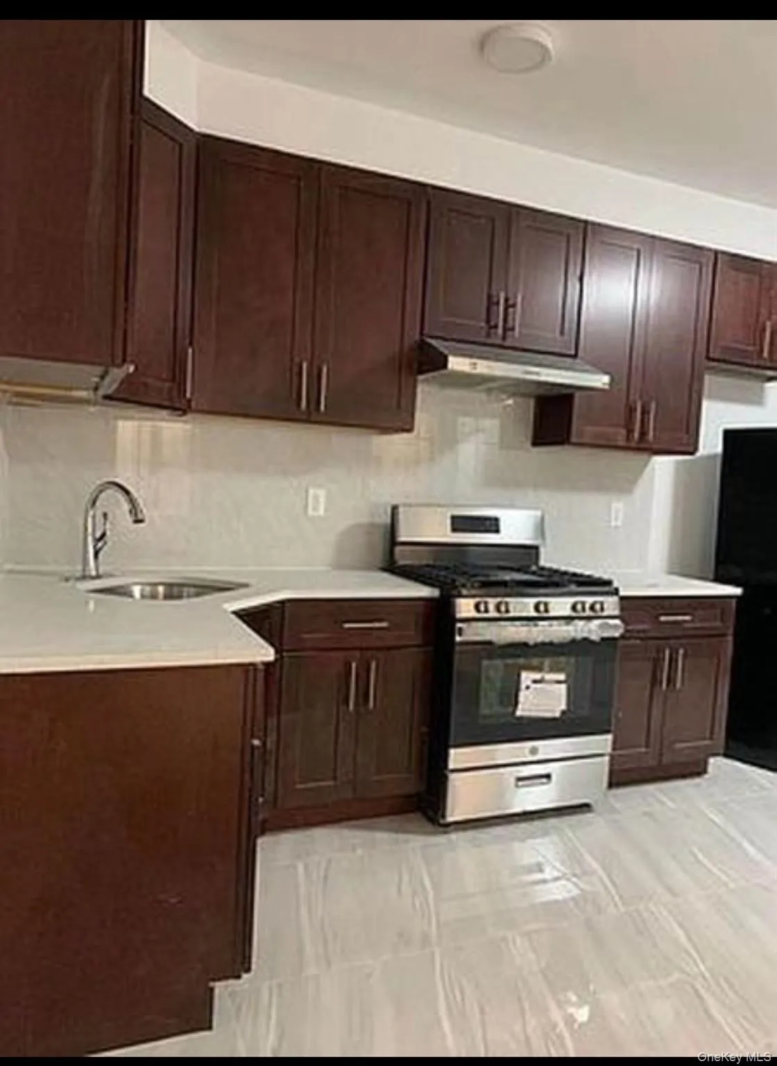 Kitchen featuring gas range, dark brown cabinetry, under cabinet range hood, freestanding refrigerator, and light stone counters Kitchen featuring gas range, dark brown cabinetry, under cabinet range hood, freestanding refrigerator, and light stone counters