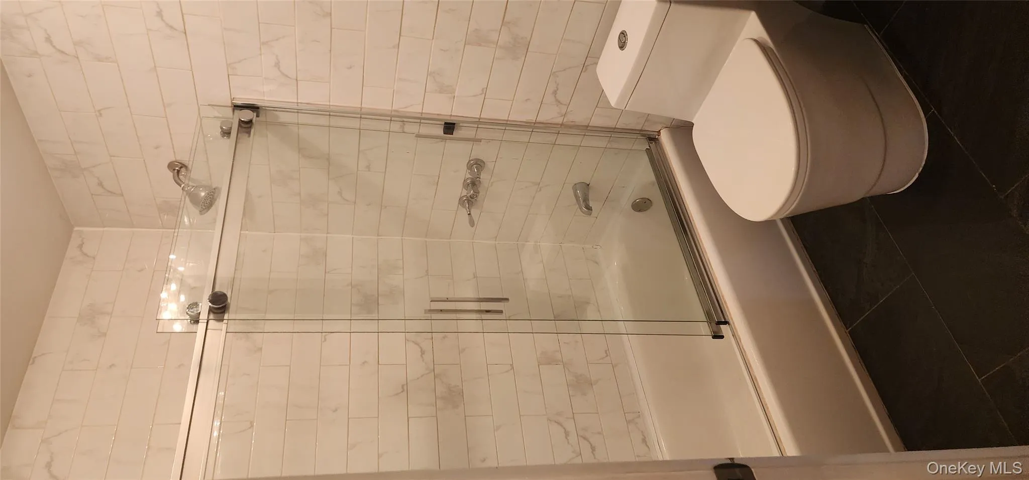 Full bath with bath / shower combo with glass door and dark tile patterned floors Full bath with bath / shower combo with glass door and dark tile patterned floors