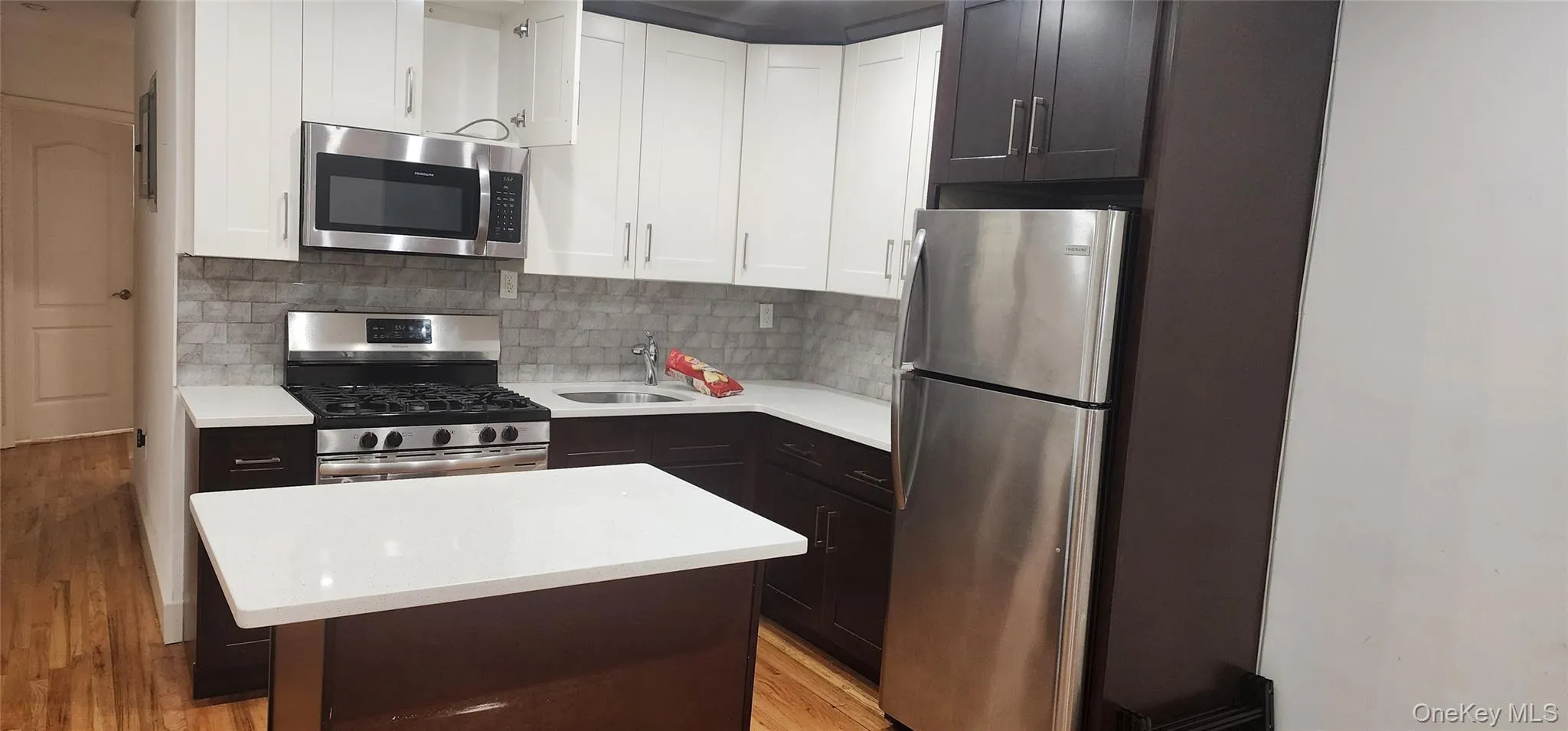 Kitchen featuring appliances with stainless steel finishes, white cabinetry, tasteful backsplash, a kitchen island, and light stone counters Kitchen featuring appliances with stainless steel finishes, white cabinetry, tasteful backsplash, a kitchen island, and light stone counters