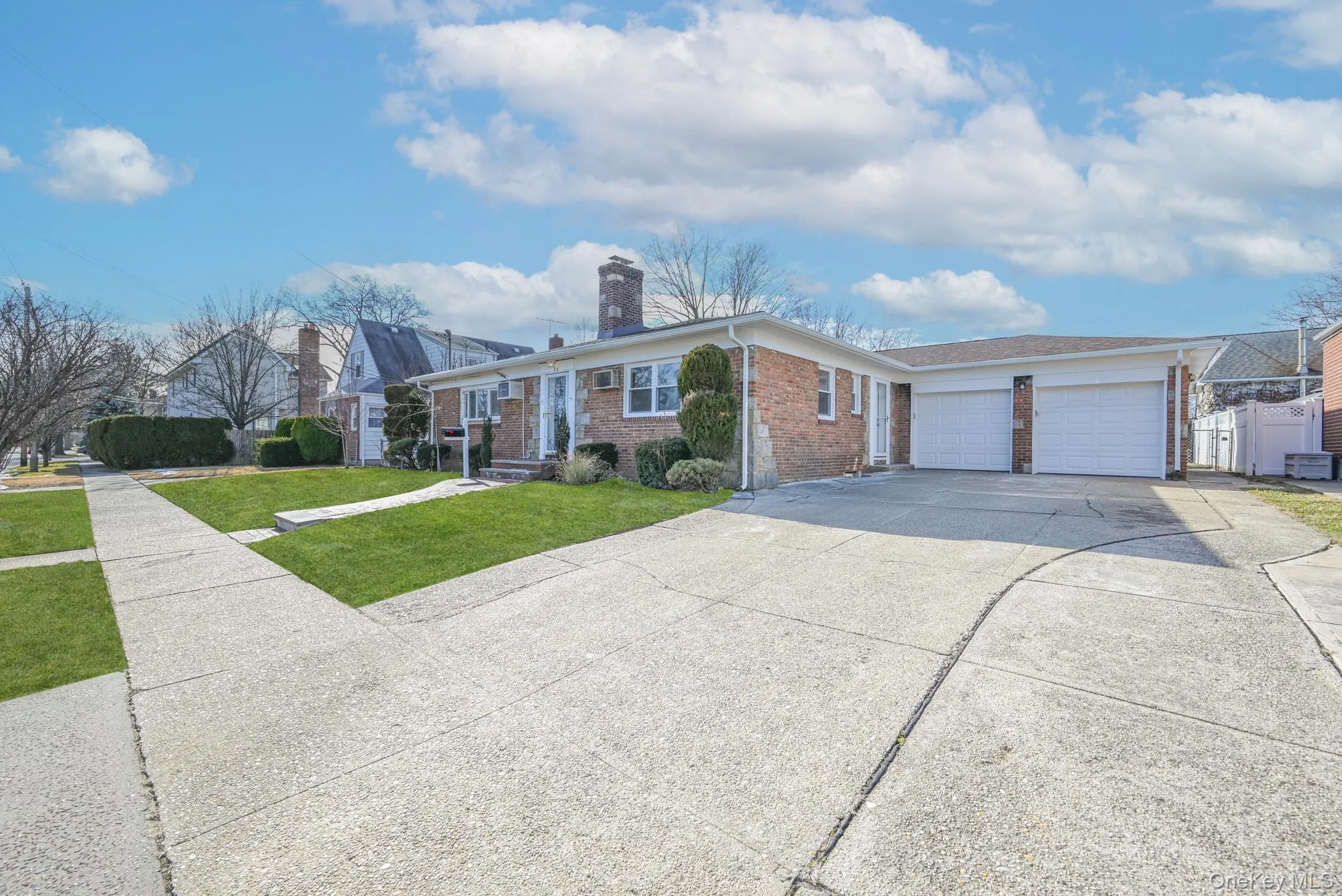 Ranch-style home featuring a front lawn, driveway, a chimney, brick siding, and an attached garage Ranch-style home featuring a front lawn, driveway, a chimney, brick siding, and an attached garage