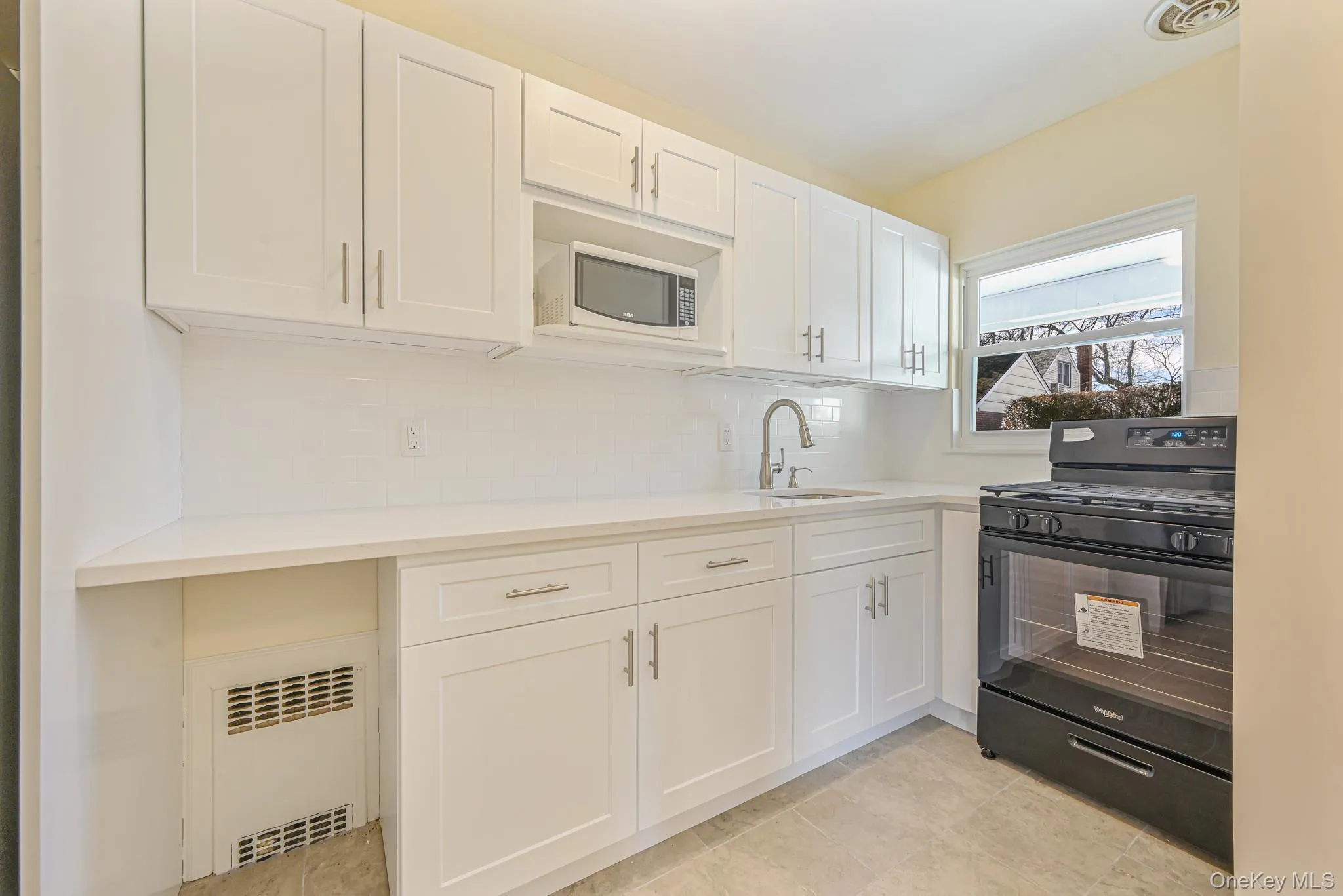 Kitchen featuring black gas stove, white cabinets, radiator heating unit, decorative backsplash, and light stone countertops Kitchen featuring black gas stove, white cabinets, radiator heating unit, decorative backsplash, and light stone countertops