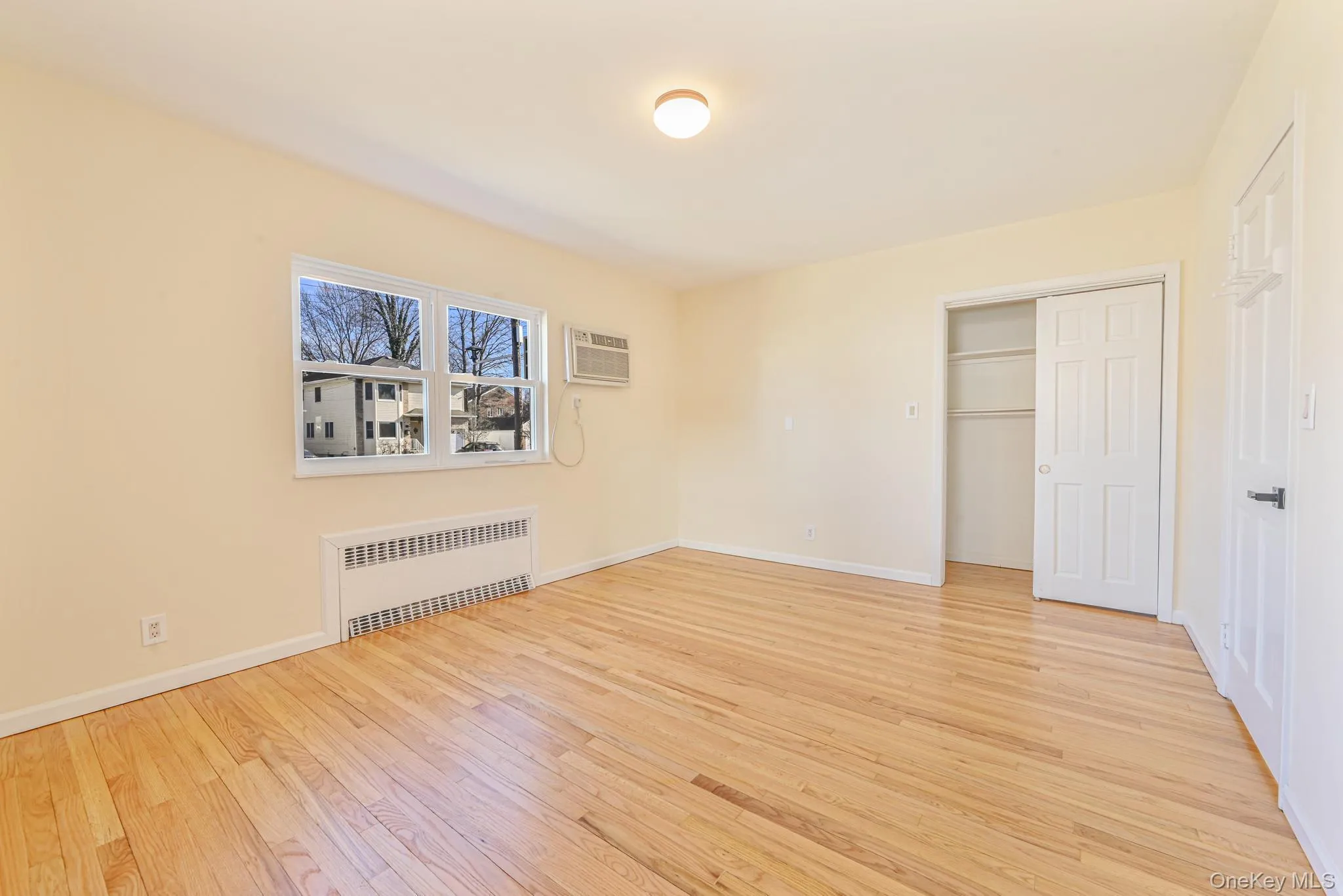 Unfurnished bedroom featuring radiator, a closet, light wood-type flooring, and a wall unit AC Unfurnished bedroom featuring radiator, a closet, light wood-type flooring, and a wall unit AC